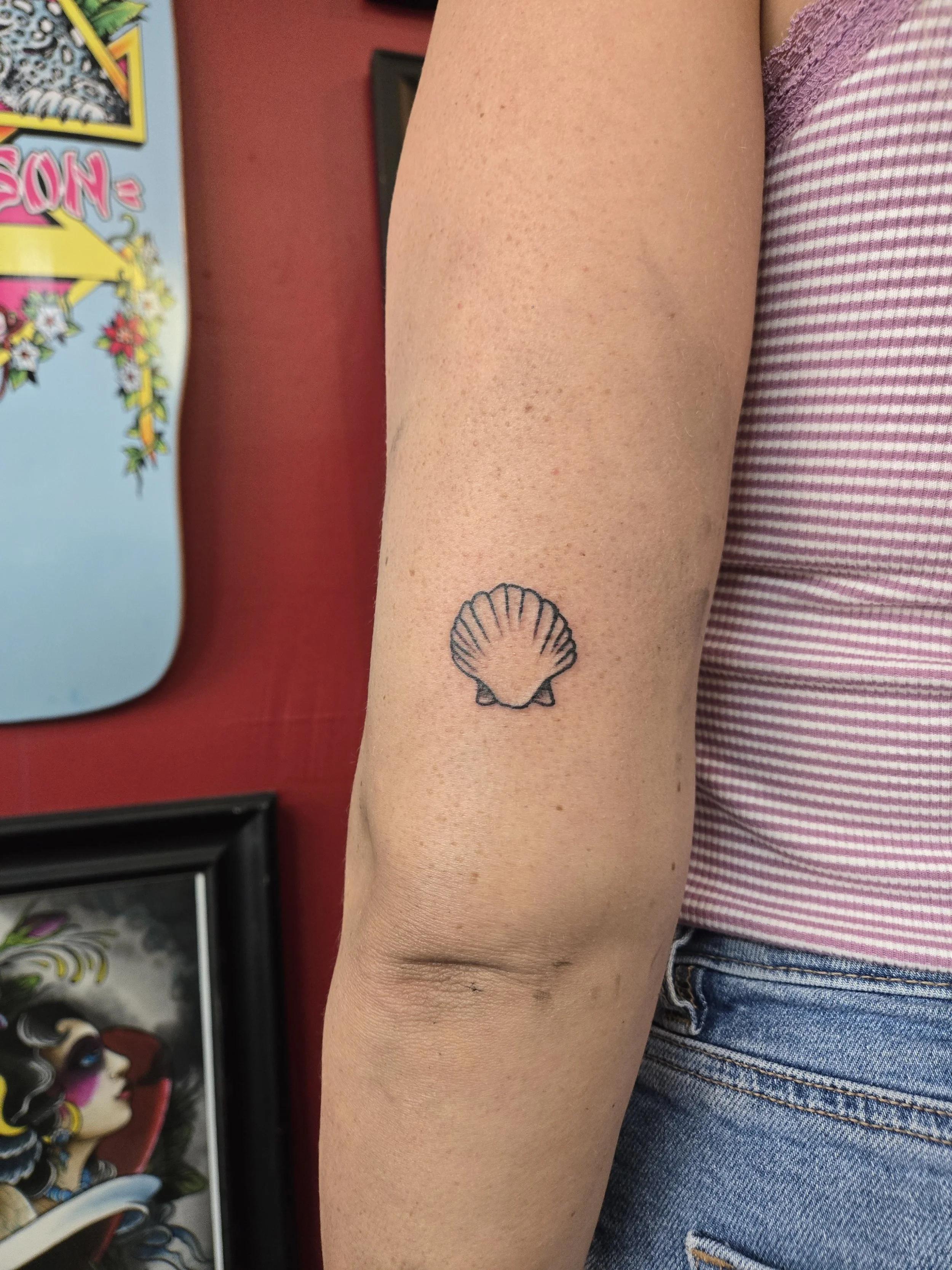 Minimalist fine line arm tattoo featuring a small scallop seashell outline with clean delicate linework, custom tattoo by Brandon Perez at Big Kahuna Tattoo in Boca Raton, FL