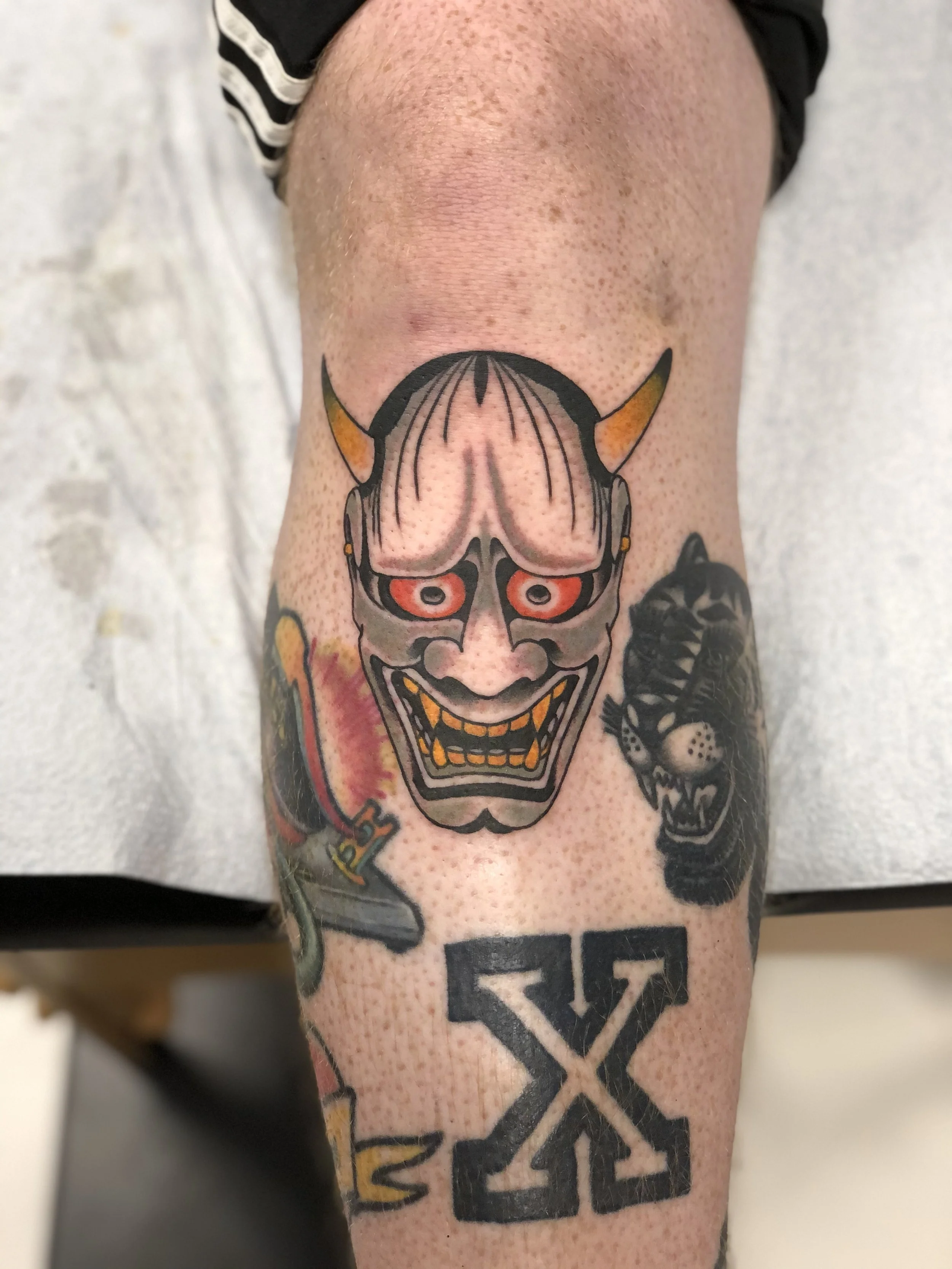 Japanese style color knee tattoo featuring a classic white and grey Hannya mask with golden horns and glowing red eyes, part of a larger leg sleeve, custom tattoo by Nick at Big Kahuna Tattoo in Boca Raton, FL.