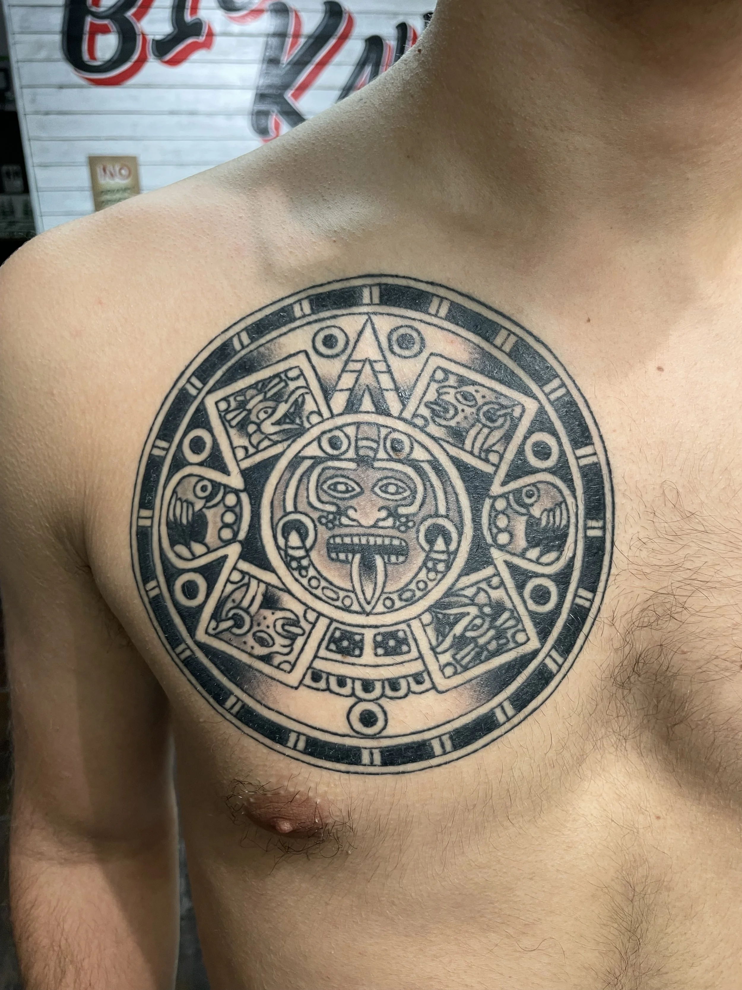 A full chest piece that commands respect. A highly detailed Mayan calendar with a central deity face, eight symbolic panels, and concentric rings of carved glyphs radiating outward. The kind of piece that takes commitment and delivers. Black and grey