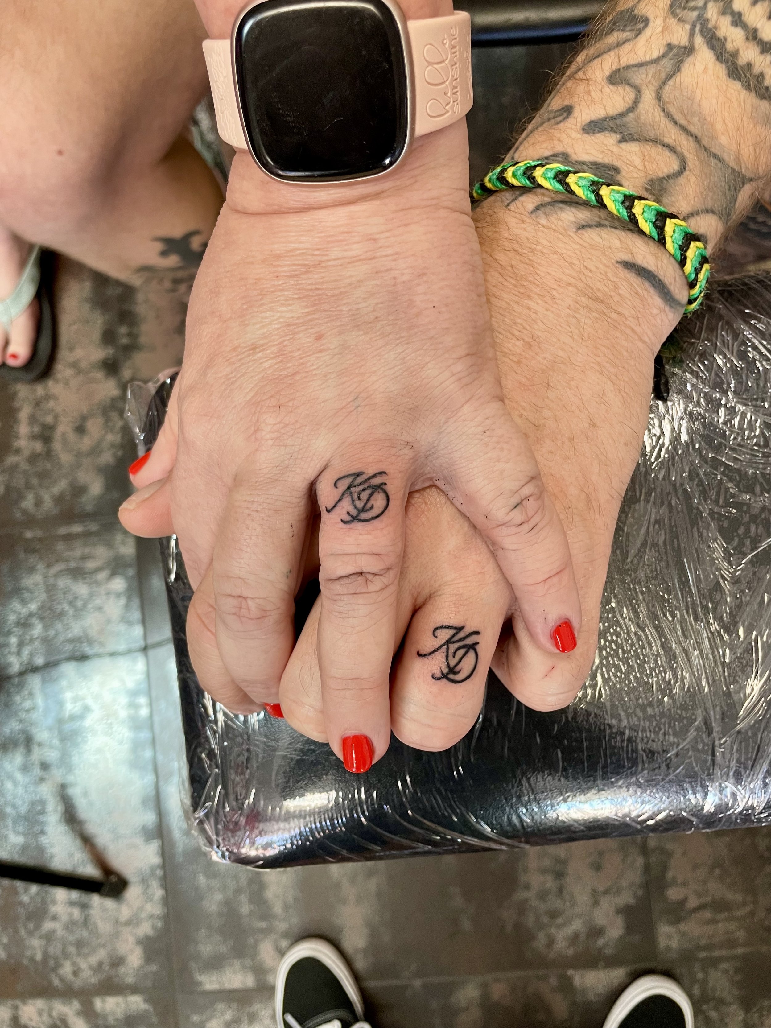 Matching fine line finger tattoos for two, featuring a pair of intertwined script initials tattooed on the ring fingers, custom matching tattoos by Nick at Big Kahuna Tattoo in Boca Raton, FL.