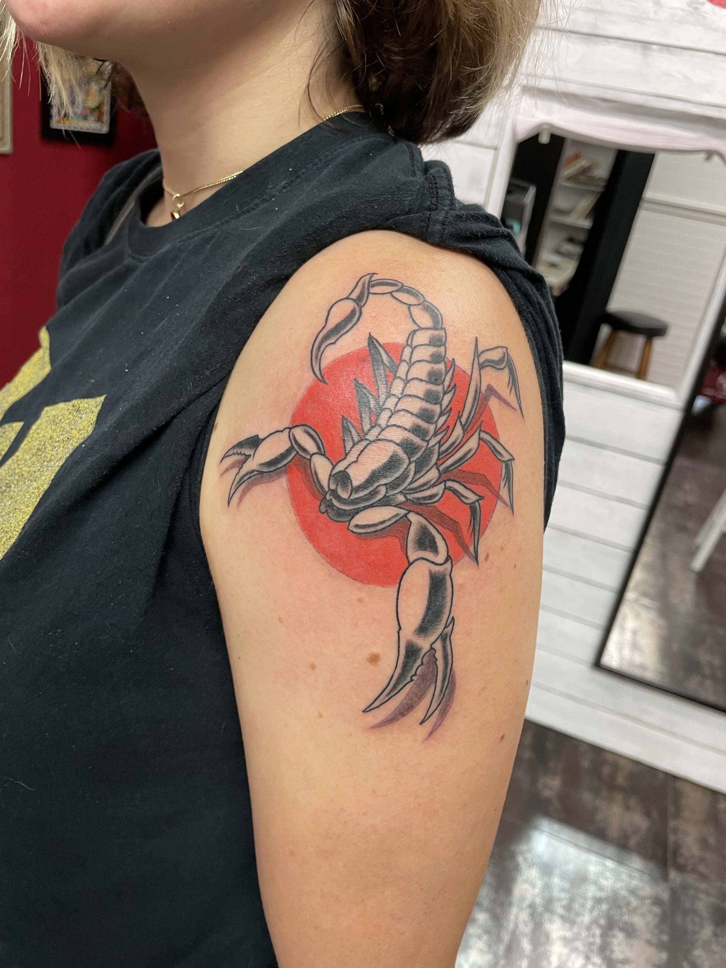 Black and grey shoulder tattoo featuring a highly detailed scorpion posed in attack position over a solid red sun circle, custom tattoo by Nick at Big Kahuna Tattoo in Boca Raton, FL.