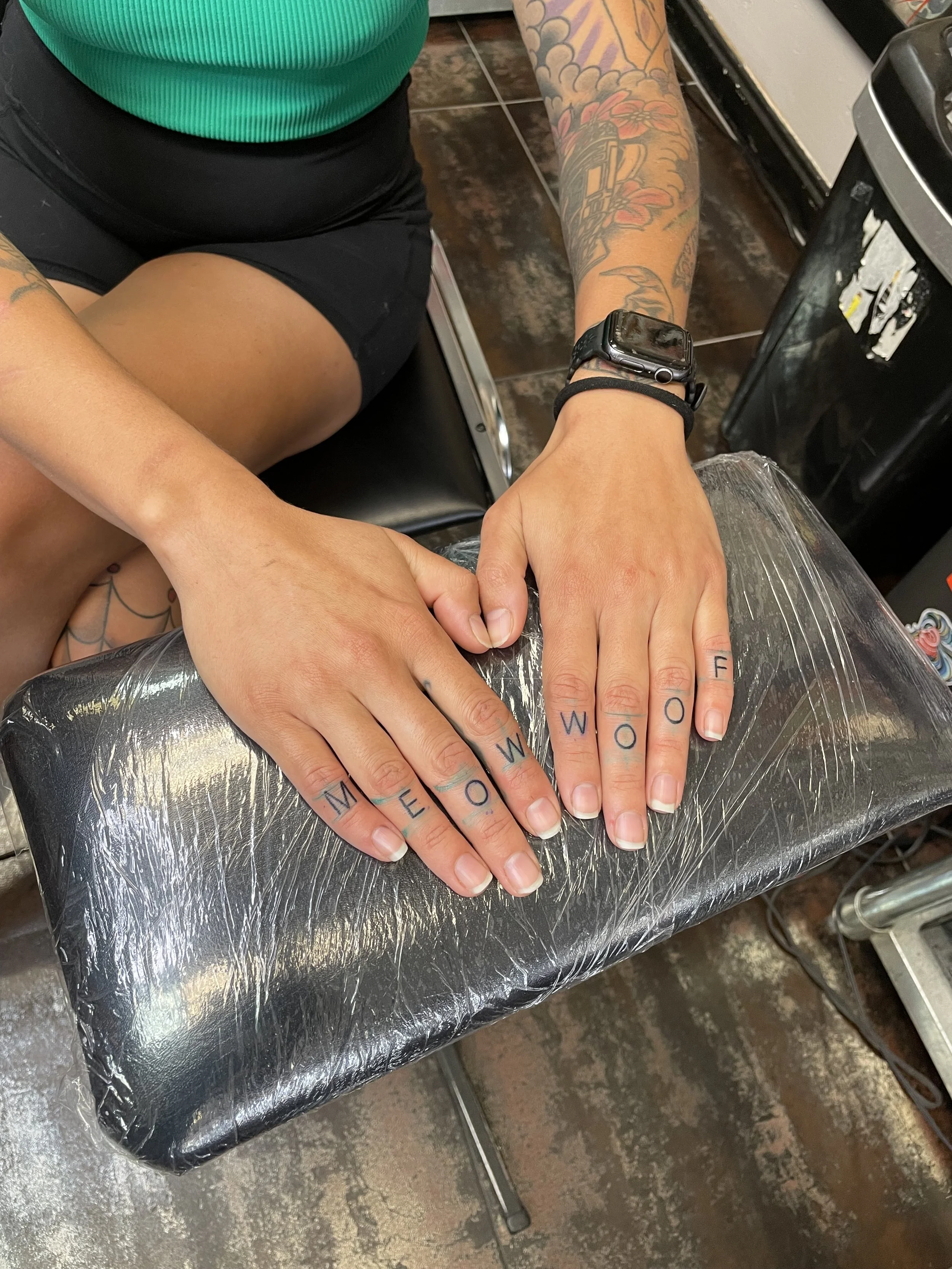Fine line finger tattoos featuring the words "Meow" and "Woof" tattooed across the knuckles of both hands in simple block lettering, custom tattoo by Nick at Big Kahuna Tattoo in Boca Raton, FL.