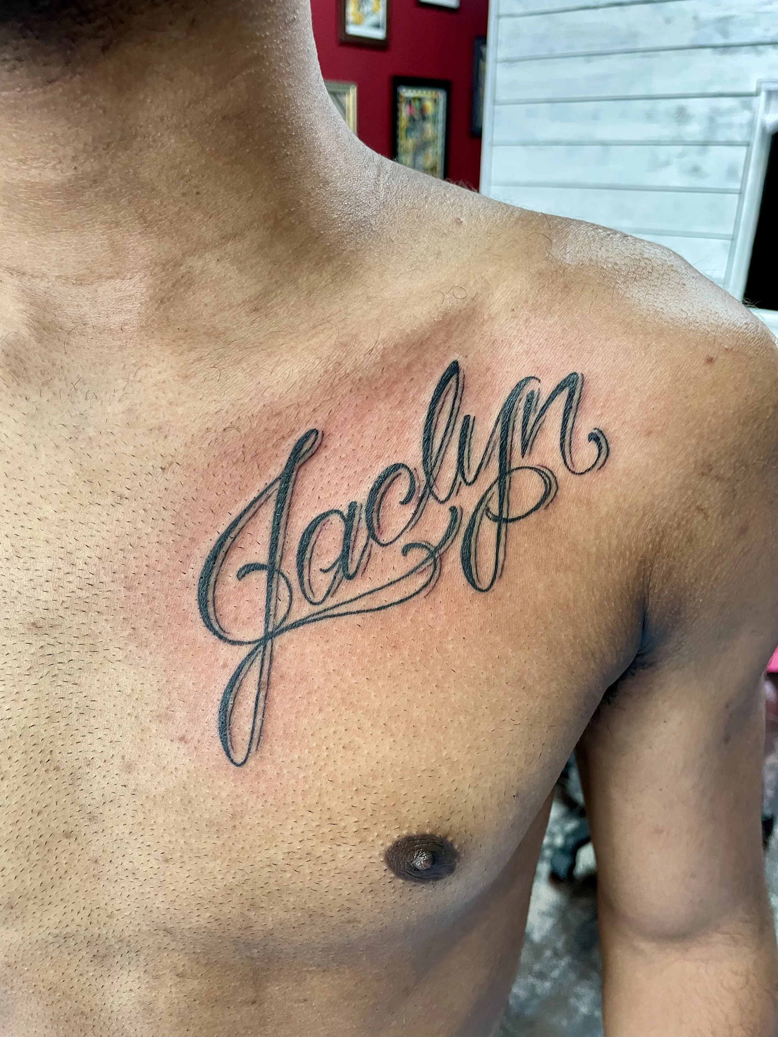 Bold script chest tattoo featuring the name "Jaclyn" in sweeping cursive lettering with long looping strokes and graceful flourishes, custom tattoo by Nick at Big Kahuna Tattoo in Boca Raton, FL.
