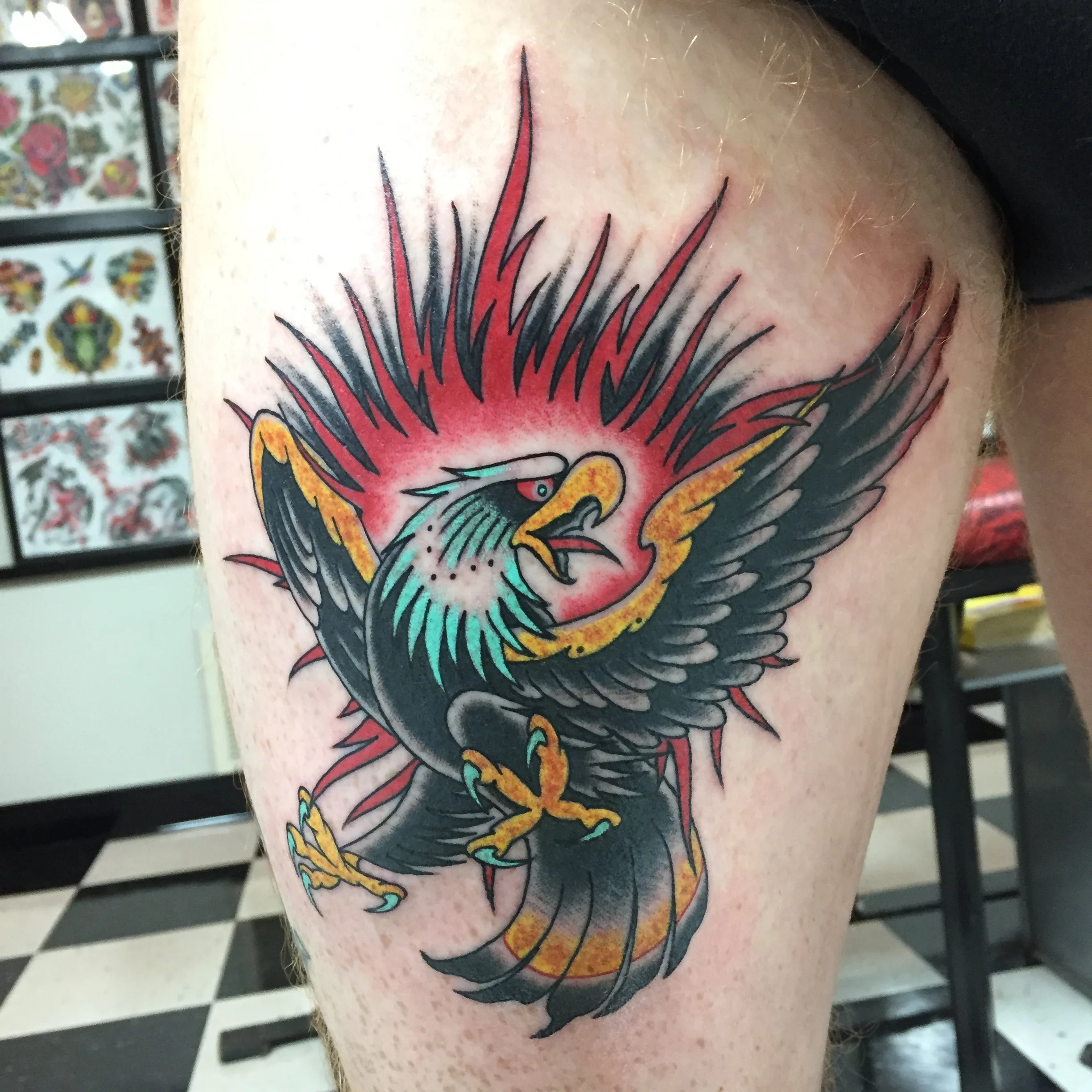 Traditional American color thigh tattoo featuring a bold screaming eagle in flight with outstretched wings surrounded by red flames, custom tattoo by Nick at Big Kahuna Tattoo in Boca Raton, FL.