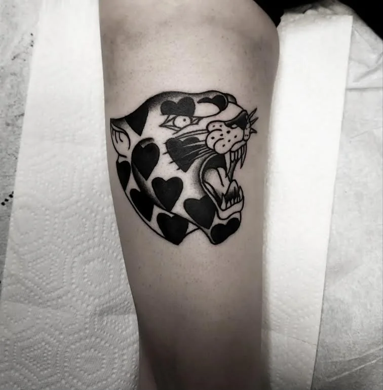 Bold black and grey traditional leg tattoo featuring a snarling panther head decorated with black heart spots, custom tattoo by Brandon Perez at Big Kahuna Tattoo in Boca Raton, FL