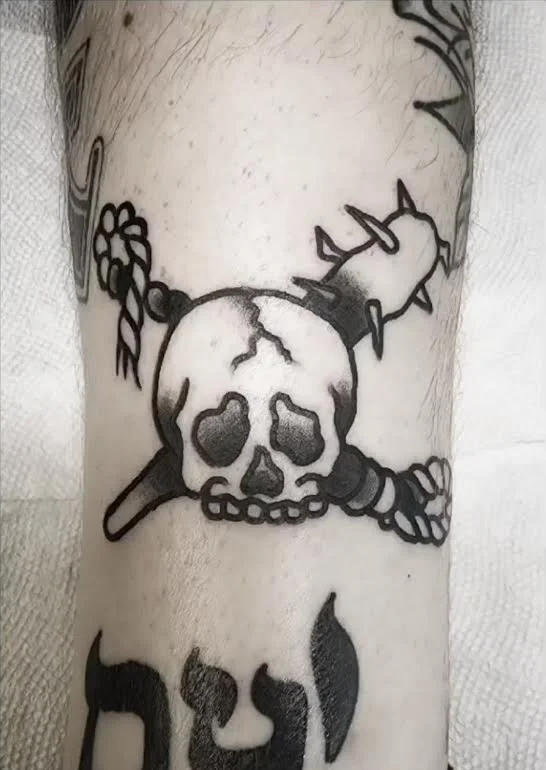 Black and grey traditional forearm tattoo featuring a bold skull and crossbones with a braided rope and spiked club, custom tattoo by Brandon Perez at Big Kahuna Tattoo in Boca Raton, FL