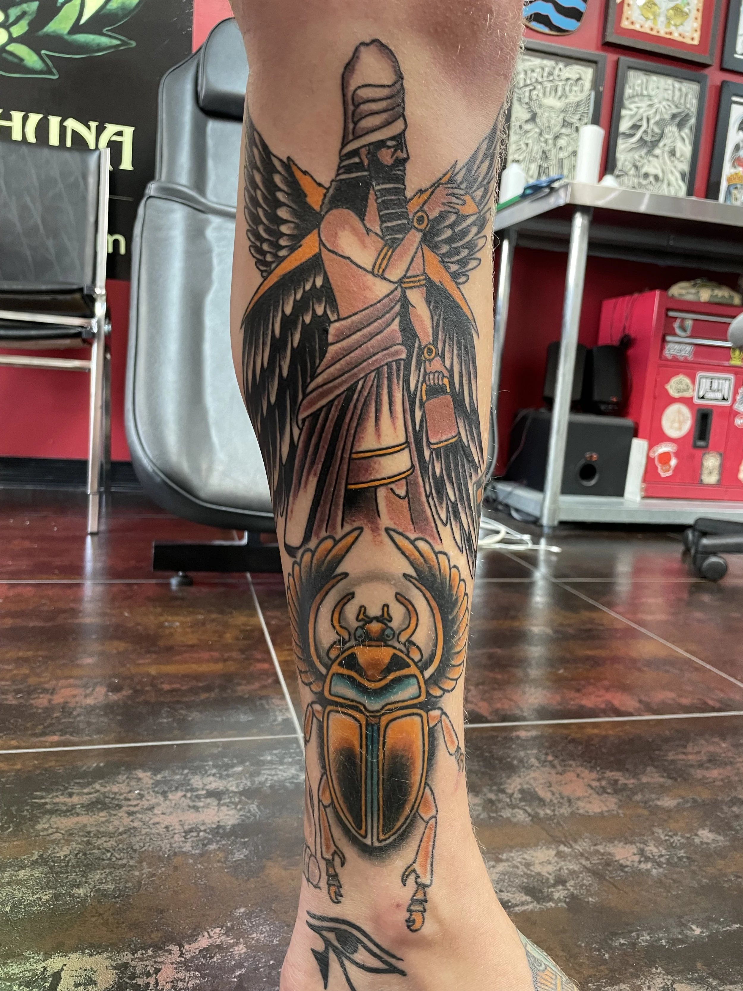 Traditional American color leg sleeve tattoo featuring a winged Anunnaki deity figure in ancient Mesopotamian style above a large detailed gold and teal scarab beetle, set as part of a larger leg composition, custom tattoo by Nick at Big Kahuna Tatto