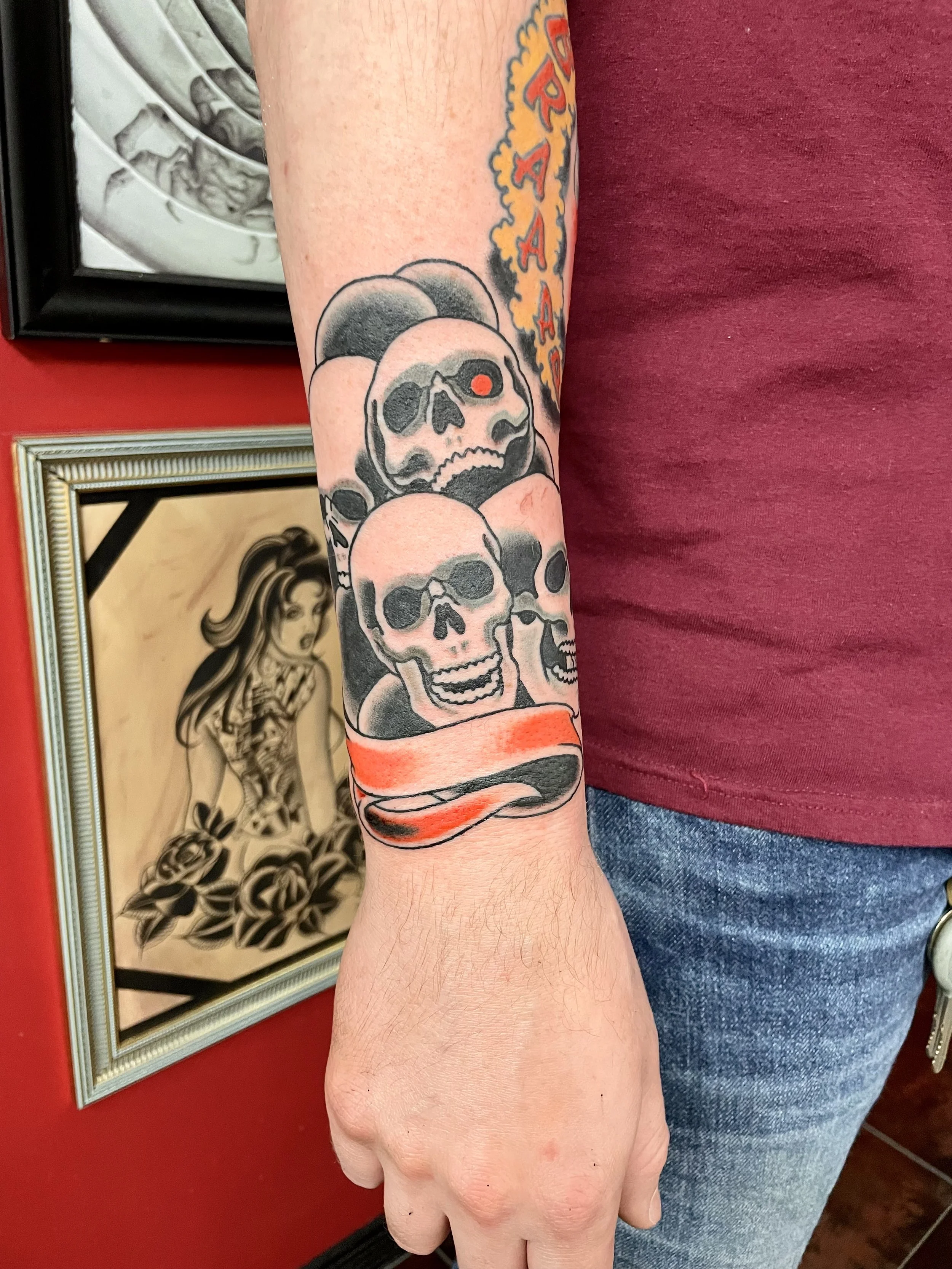 Traditional American black and grey wrist tattoo featuring a pile of skulls with a bold red scroll banner below, custom tattoo by Nick at Big Kahuna Tattoo in Boca Raton, FL.