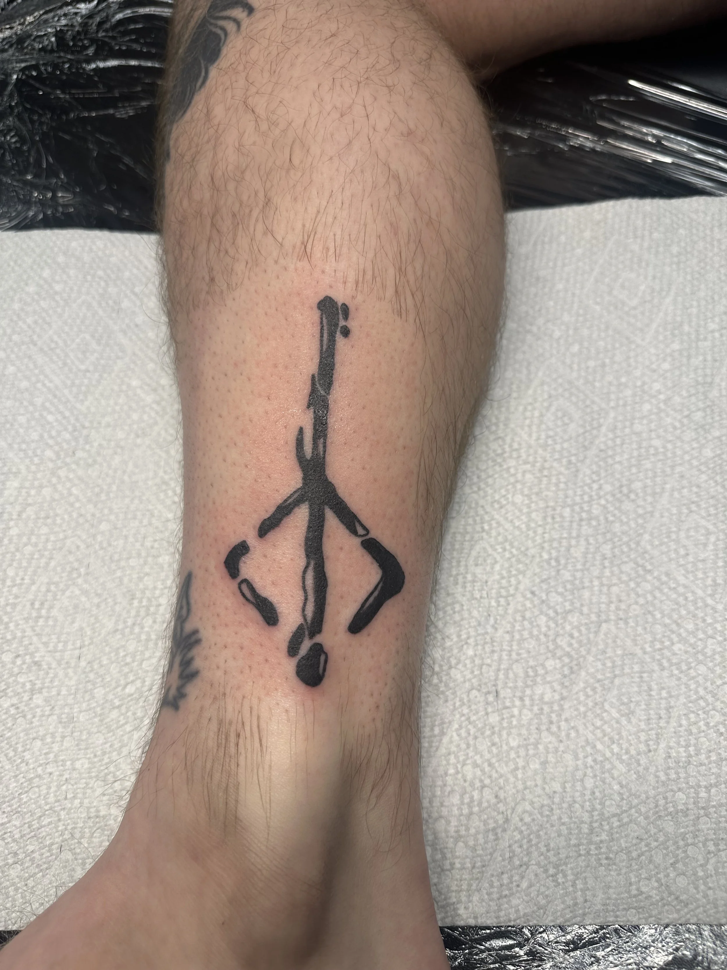 Black and grey ankle tattoo featuring a bold rune symbol in a carved in stone style with heavy black ink, custom tattoo by Dan at Big Kahuna Tattoo in Boca Raton, FL.