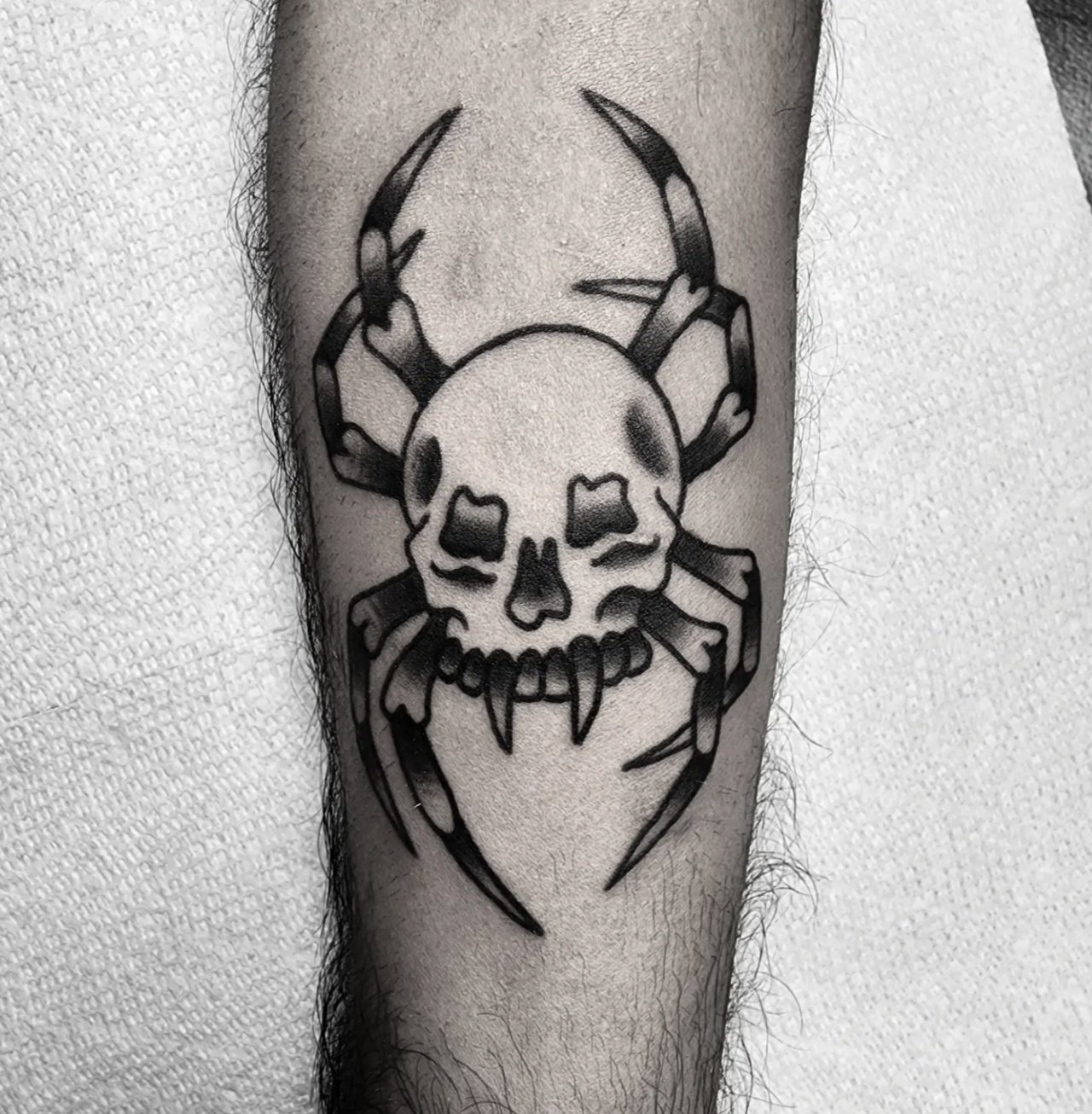 Bold black and grey traditional forearm tattoo featuring a creative skull and spider hybrid design with curved spider legs surrounding a snarling skull face, custom tattoo by Brandon Perez at Big Kahuna Tattoo in Boca Raton, FL