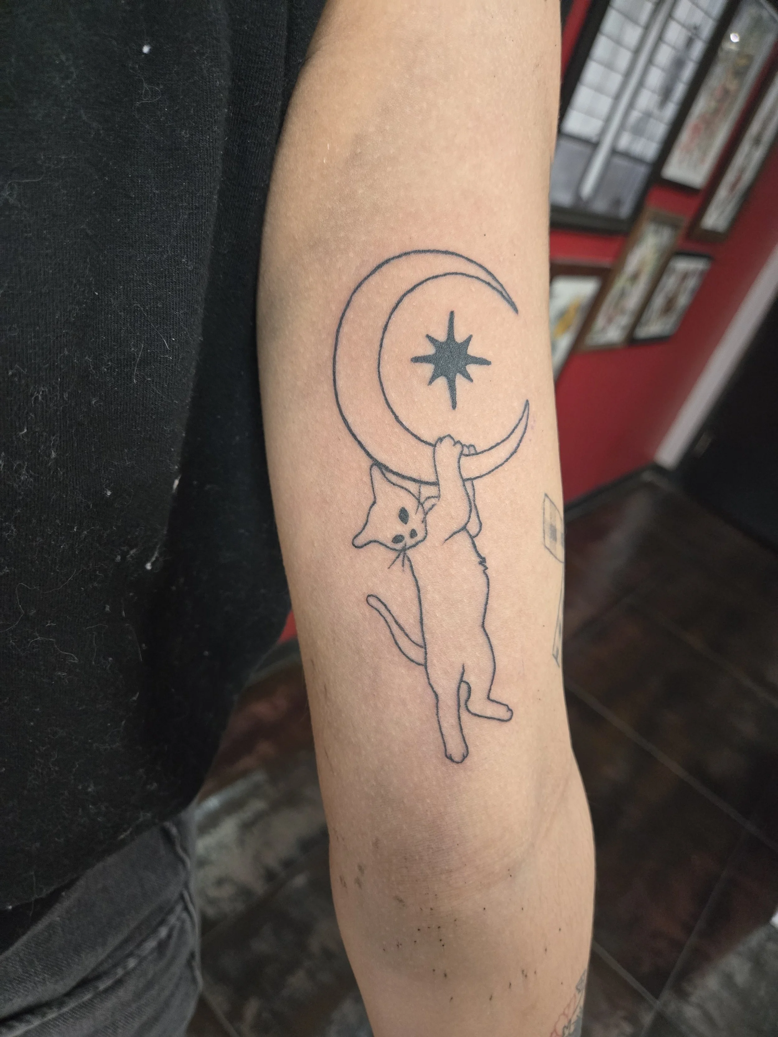 Fine line forearm tattoo featuring a minimalist cat hanging from a crescent moon with a north star, custom tattoo by Brandon Perez at Big Kahuna Tattoo in Boca Raton, FL