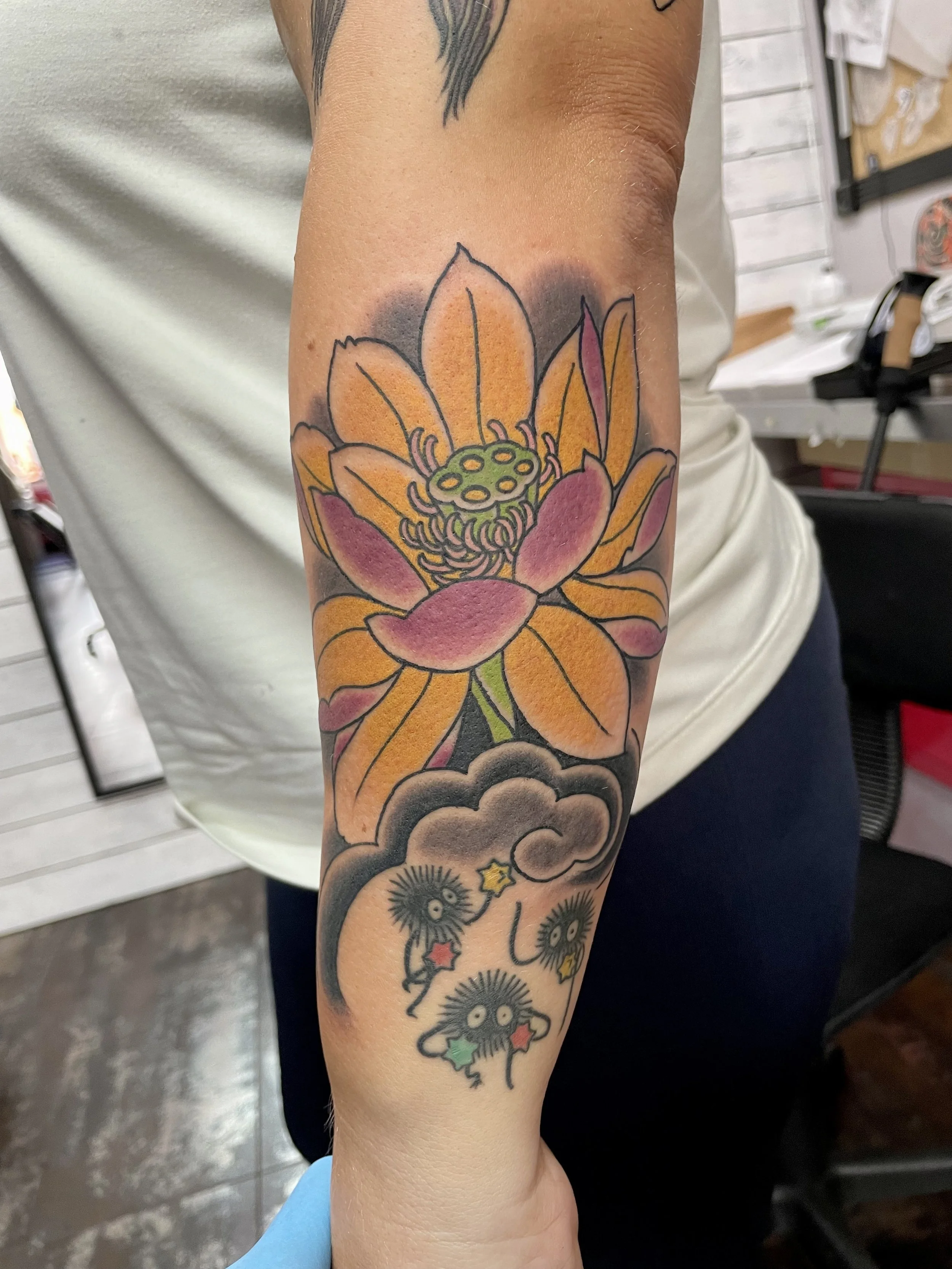 A large golden and pink lotus floats above a dark cloud from which Studio Ghibli's beloved soot sprites peek out clutching colorful stars. A playful collision of Japanese traditional and anime culture that only works because it's drawn with care. Jap