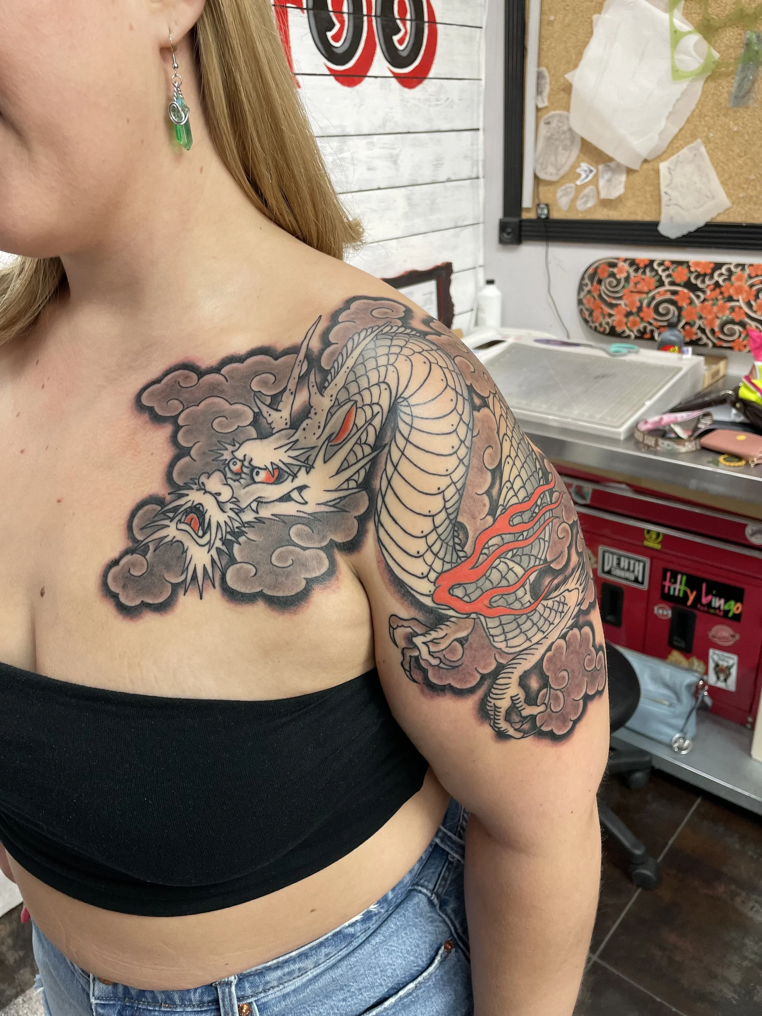 Japanese black and grey color dragon shoulder and chest tattoo featuring a fierce white dragon with vivid red eyes and red flame accents coiling across the shoulder and onto the chest, surrounded by billowing dark storm clouds, custom tattoo by Nick 