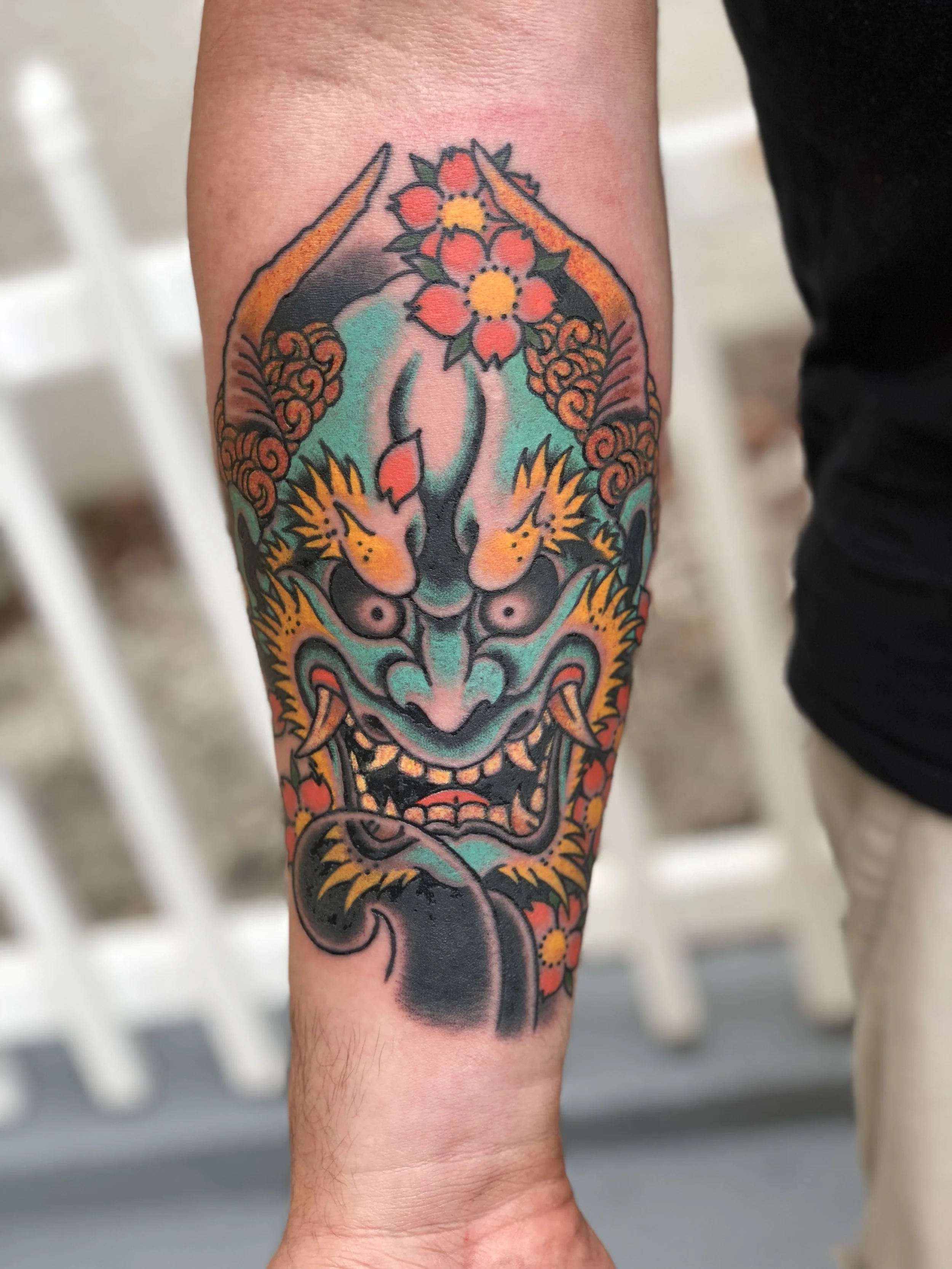 Japanese style color forearm tattoo featuring a teal Oni mask with gold detailing, red cherry blossoms, and decorative clouds, custom tattoo by Nick at Big Kahuna Tattoo in Boca Raton, FL.