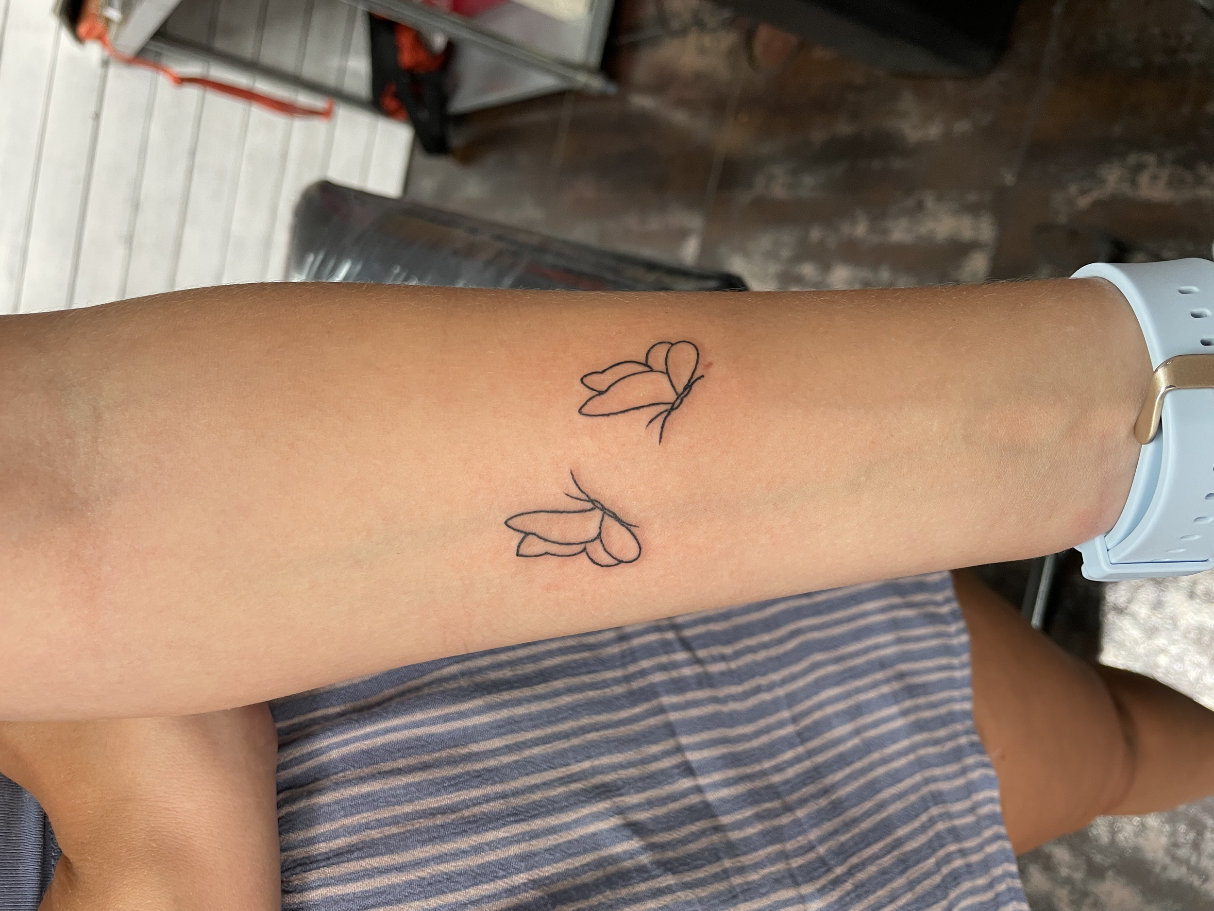Tiny fine line forearm tattoo featuring two minimalist butterfly outlines in a simple single stroke style, custom tattoo by Nick at Big Kahuna Tattoo in Boca Raton, FL.