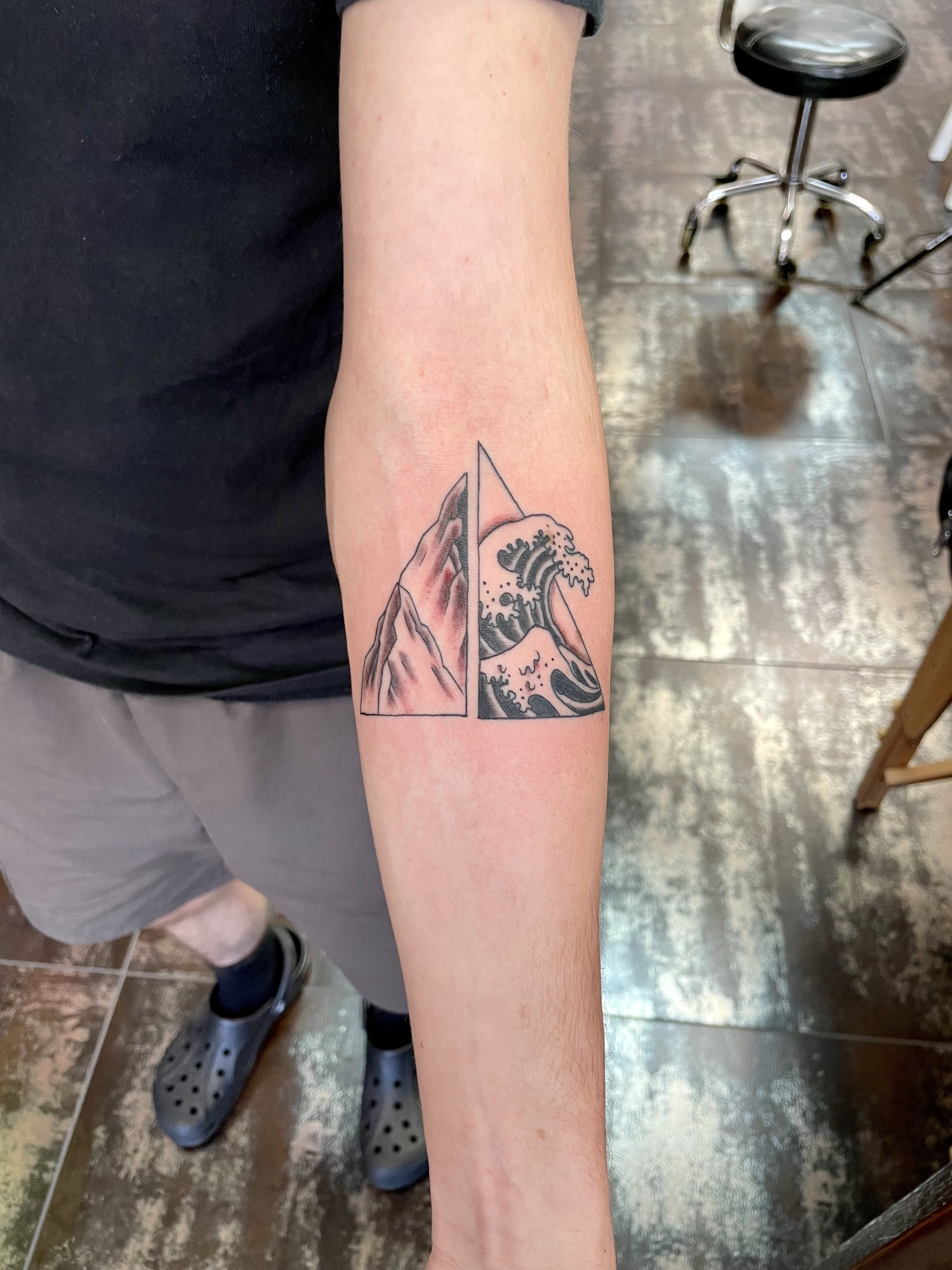 Fine line forearm tattoo featuring a geometric triangle split down the center, with a detailed mountain landscape on the left half and a bold Japanese-style crashing wave on the right, custom tattoo by Nick at Big Kahuna Tattoo in Boca Raton, FL.
