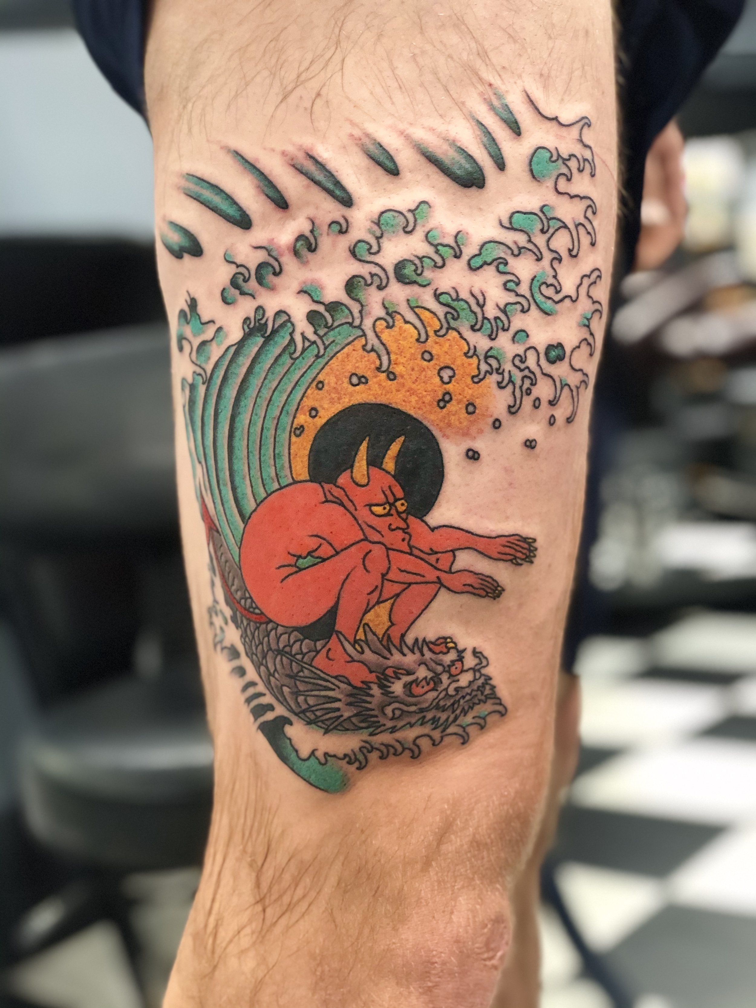 Traditional American color leg tattoo featuring a tribute to Ed Hardy's iconic "Surfin' Satan" painting, depicting a red devil riding a dragon through a Japanese style wave with an orange sun, custom tattoo by Nick at Big Kahuna Tattoo in Boca Raton,