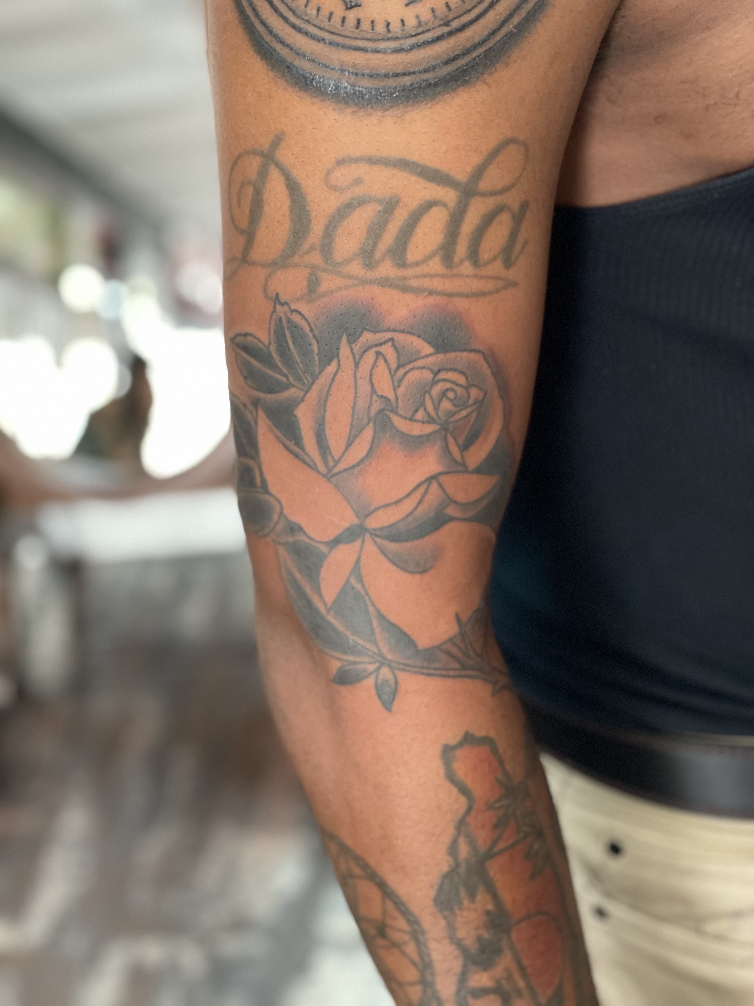 Black and grey forearm tattoo featuring a realistic rose in full bloom with leaves and a budding stem, part of a larger sleeve, custom tattoo by Nick at Big Kahuna Tattoo in Boca Raton, FL.