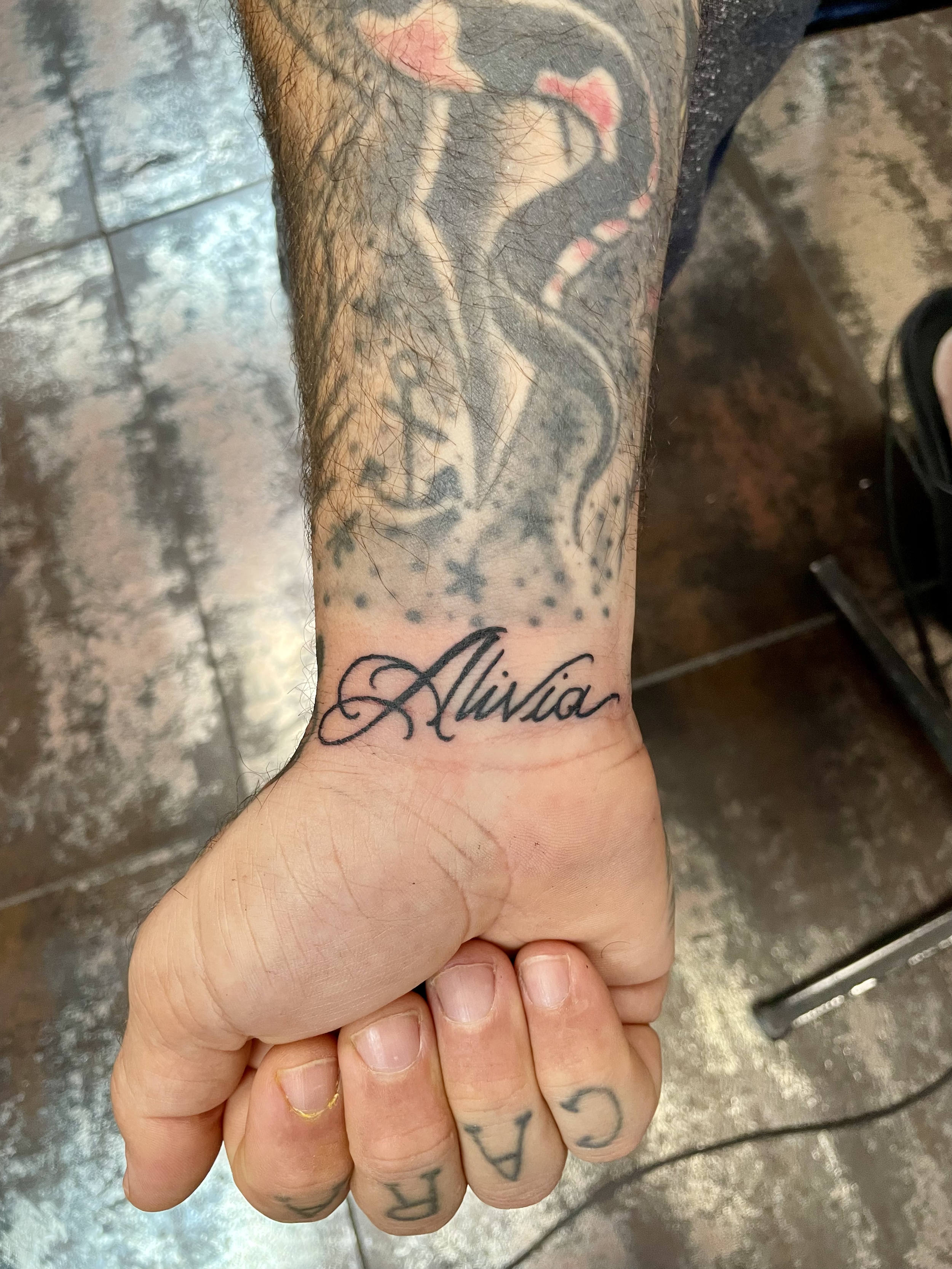Fine line cursive script wrist tattoo featuring the name "Alivia" in elegant ornate lettering, custom tattoo by Nick at Big Kahuna Tattoo in Boca Raton, FL.