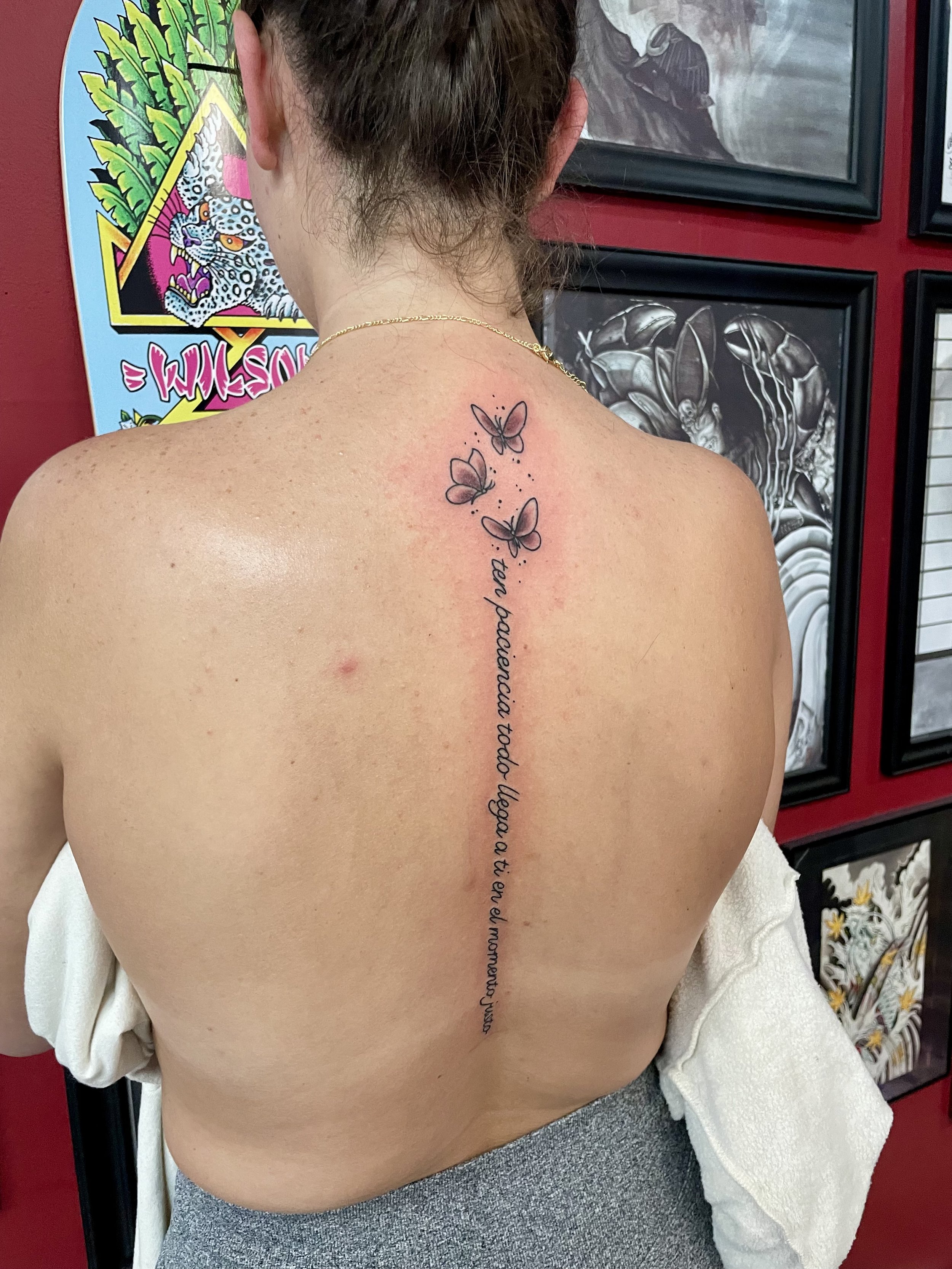 Fine line spine tattoo featuring three small ascending butterflies at the top transitioning into a long flowing Spanish script quote running the full length of the spine, custom tattoo by Nick at Big Kahuna Tattoo in Boca Raton, FL.