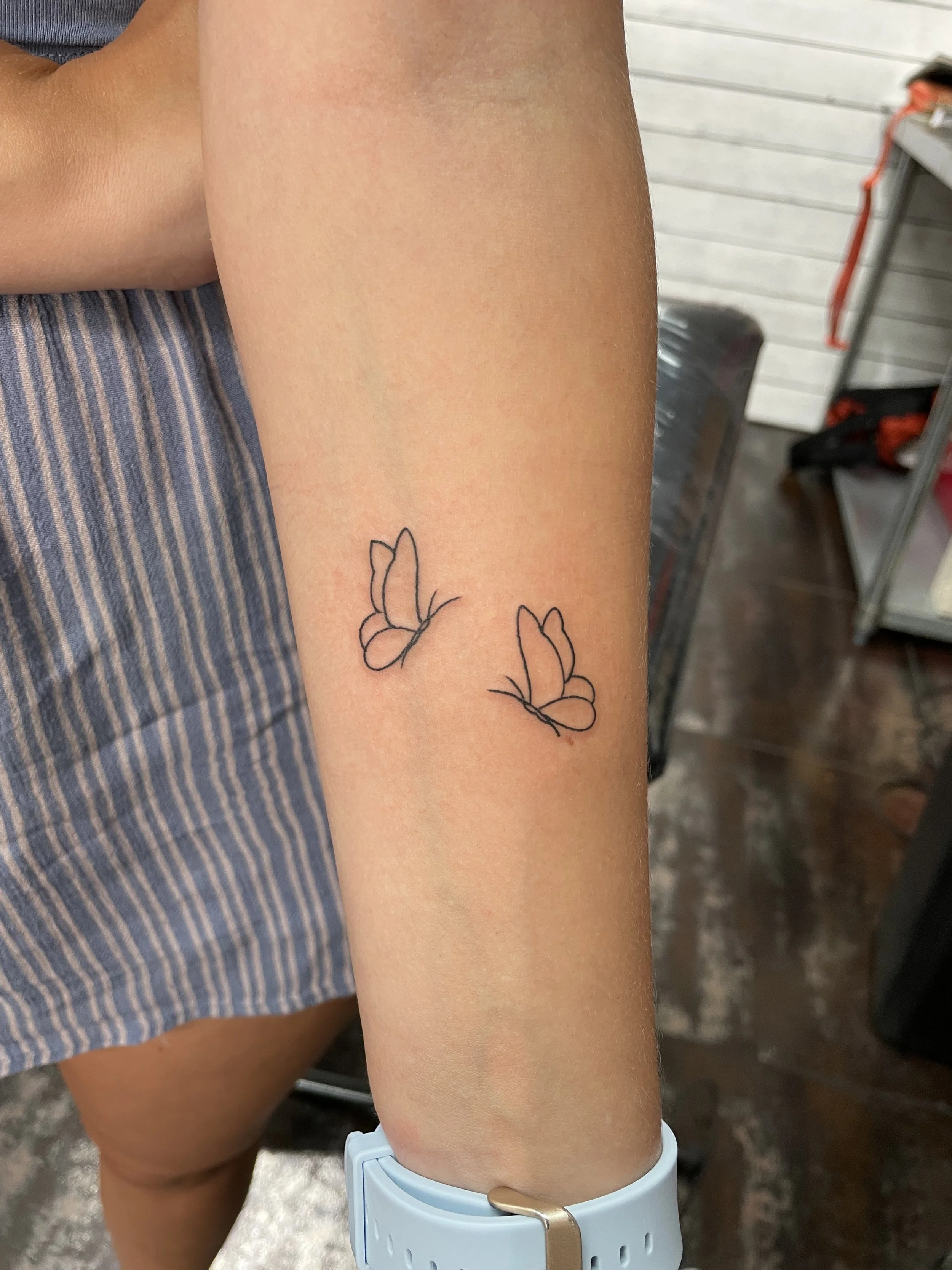 Fine line forearm tattoo featuring two small minimalist butterfly outlines in flight, positioned side by side on the inner forearm, custom tattoo by Nick at Big Kahuna Tattoo in Boca Raton, FL.