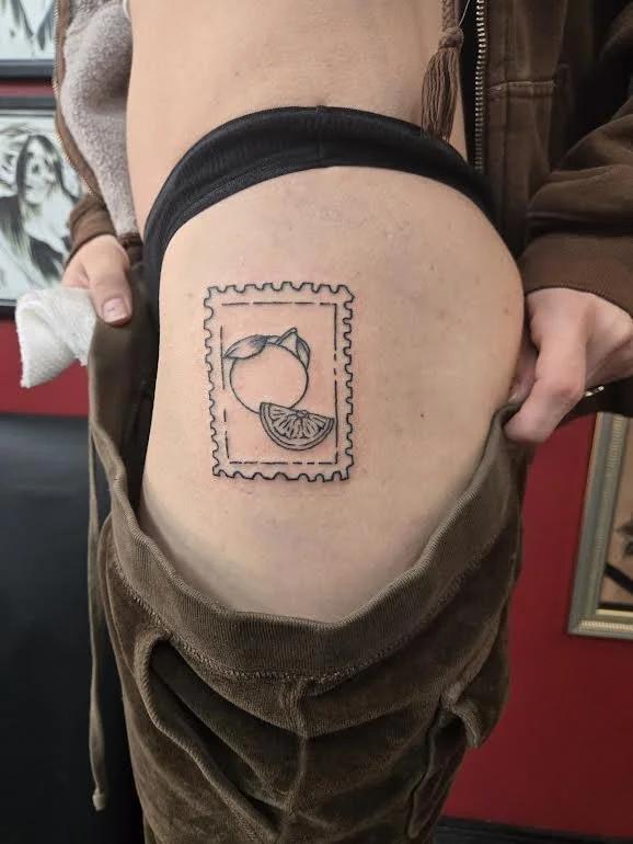 Fine line rib tattoo featuring a minimalist postage stamp design with an orange and citrus slice, custom tattoo by Brandon Perez at Big Kahuna Tattoo in Boca Raton, FL