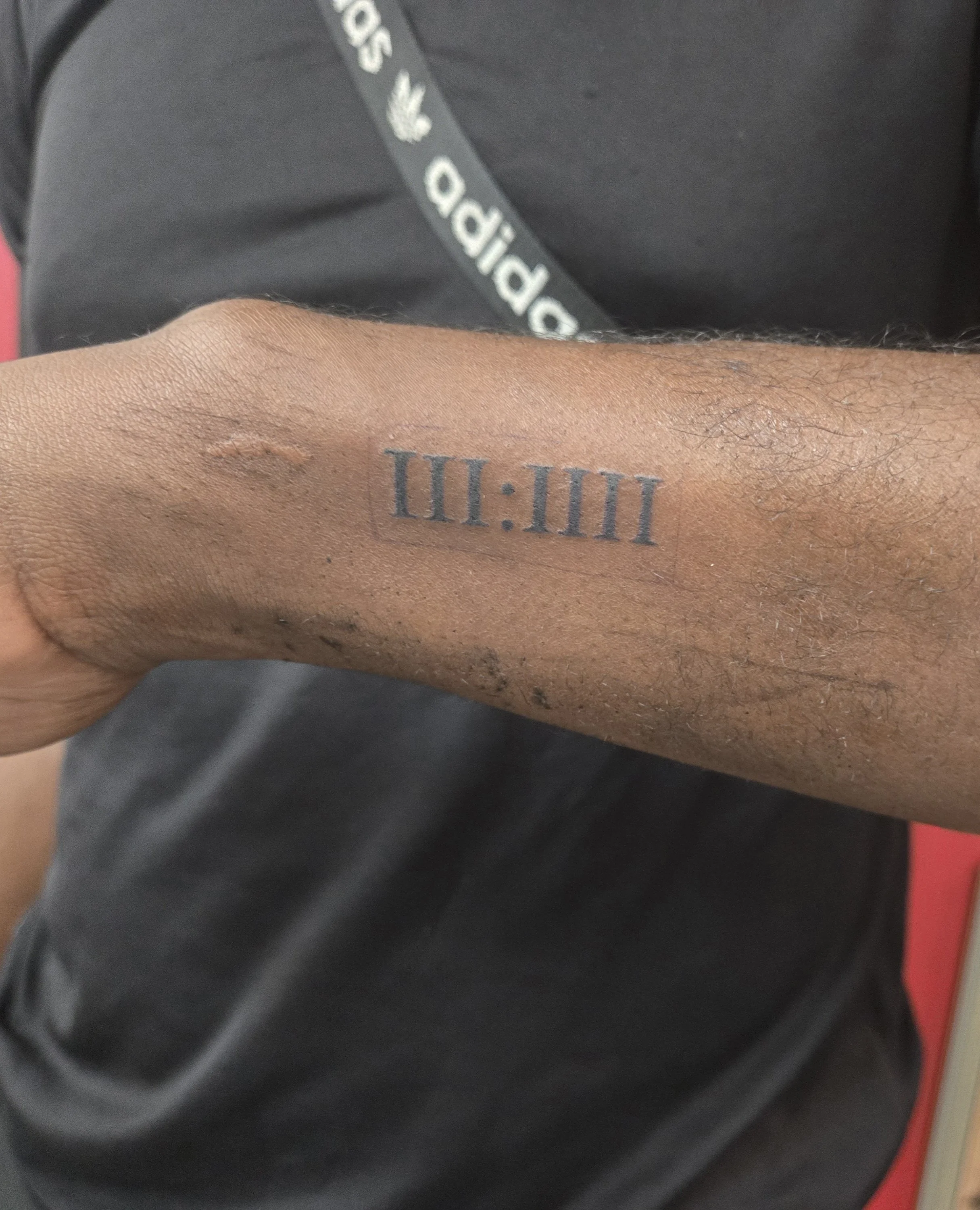 Fine line forearm tattoo featuring bold Roman numerals III:IIII in a clean serif font enclosed in a minimal rectangle, custom date tattoo by Brandon Perez at Big Kahuna Tattoo in Boca Raton, FL