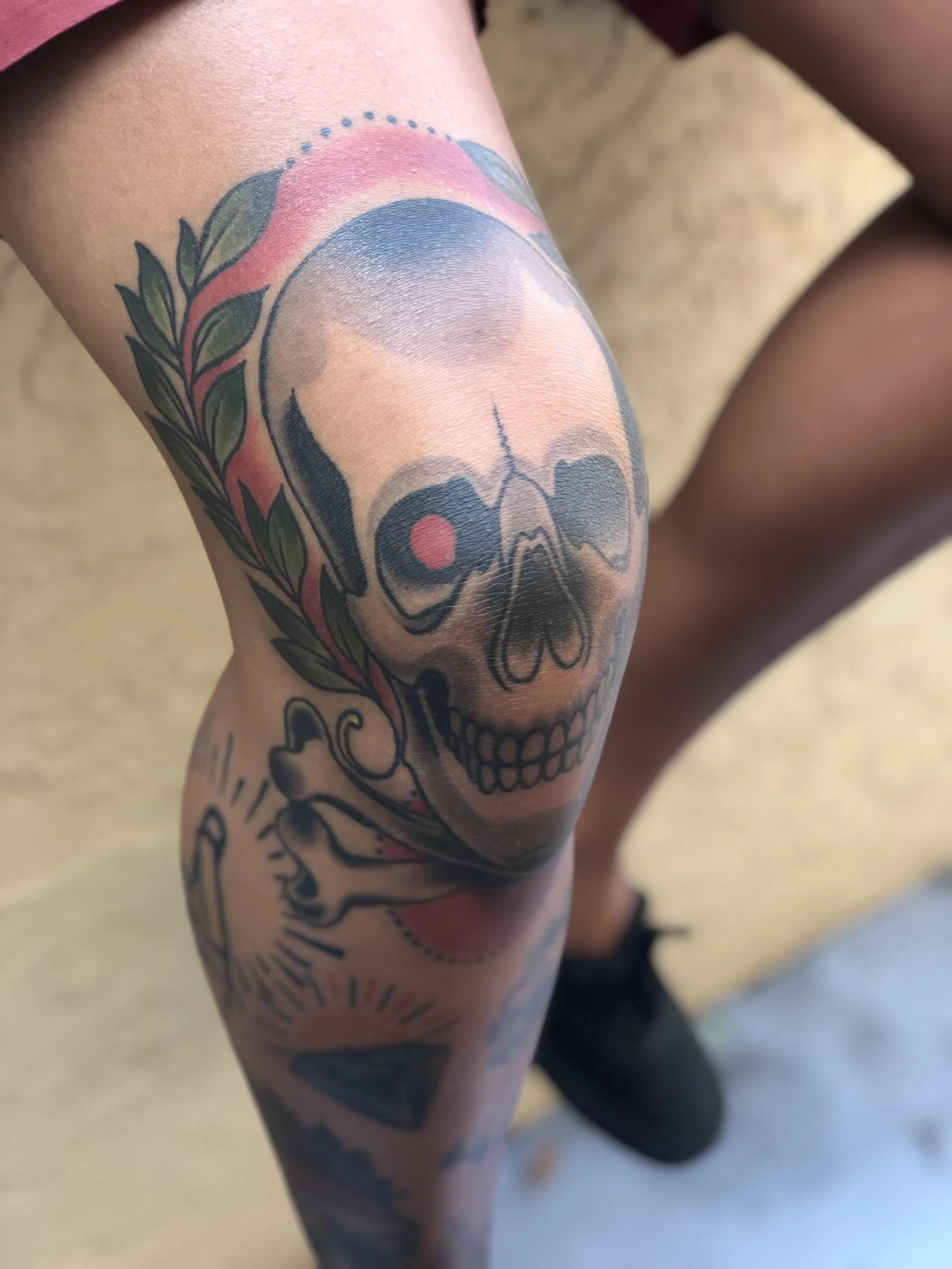 Traditional American color knee tattoo featuring a bold skull with a red eye socket and olive branch, incorporating the kneecap as the skull itself, custom tattoo by Nick at Big Kahuna Tattoo in Boca Raton, FL.