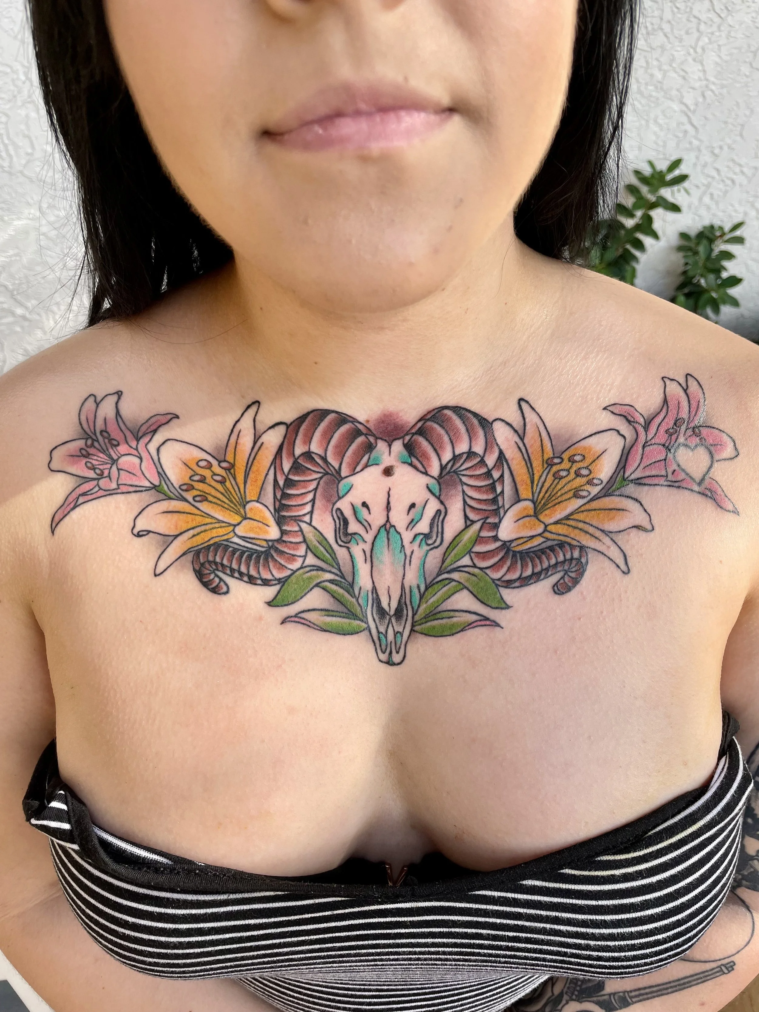 
Color chest tattoo featuring a ram skull with large curling horns and teal accent markings, flanked symmetrically by blooming tiger lilies in pink and orange with green foliage, custom tattoo by Nick at Big Kahuna Tattoo in Boca Raton, FL.