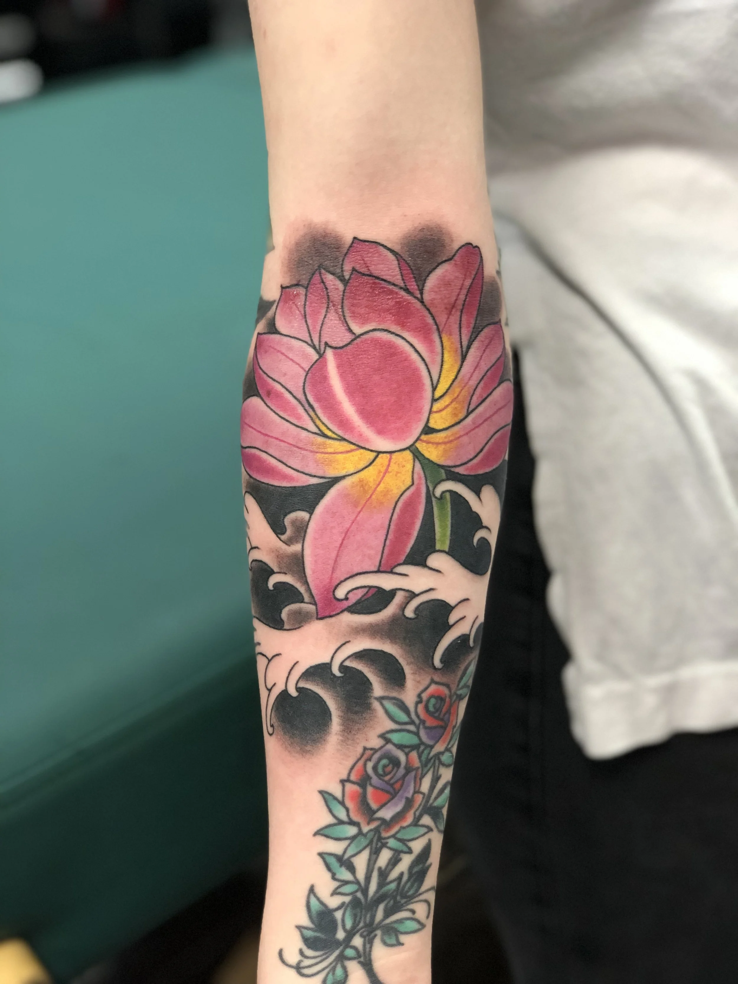 Japanese style color forearm tattoo featuring a large pink and yellow lotus flower rising from dark water with bold black wave detailing, custom tattoo by Nick at Big Kahuna Tattoo in Boca Raton, FL.