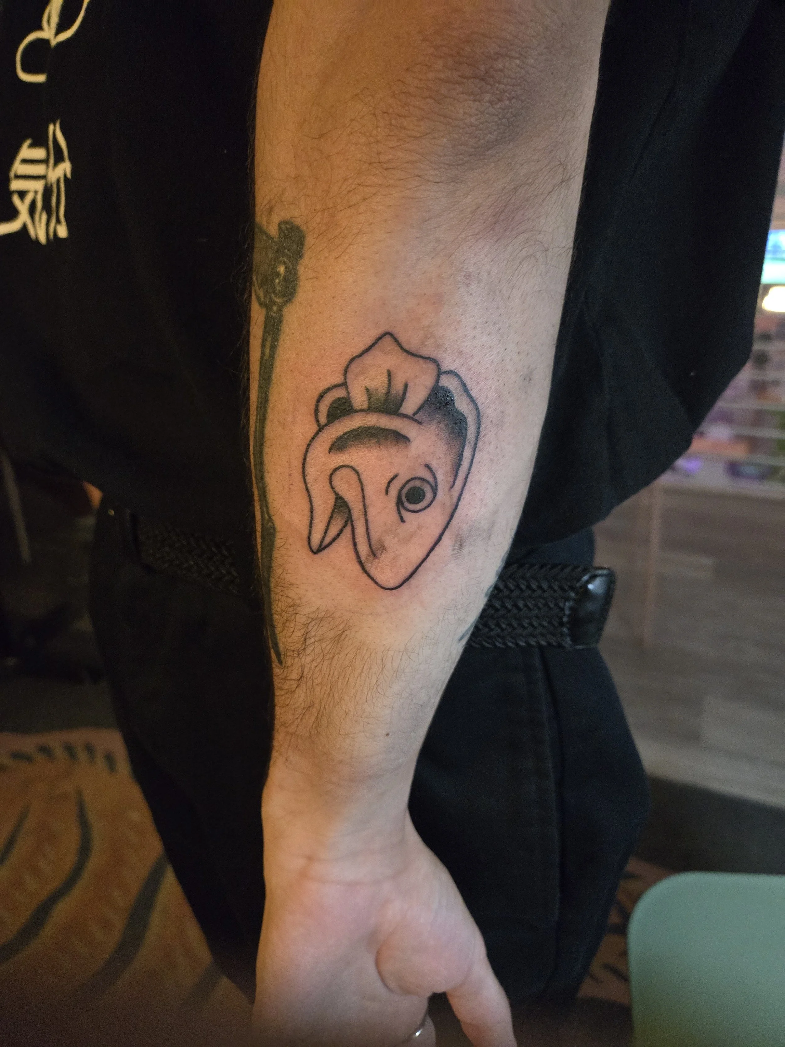 Black and grey traditional forearm tattoo featuring a bold cartoon fish head with expressive linework, custom tattoo by Brandon Perez at Big Kahuna Tattoo in Boca Raton, FL