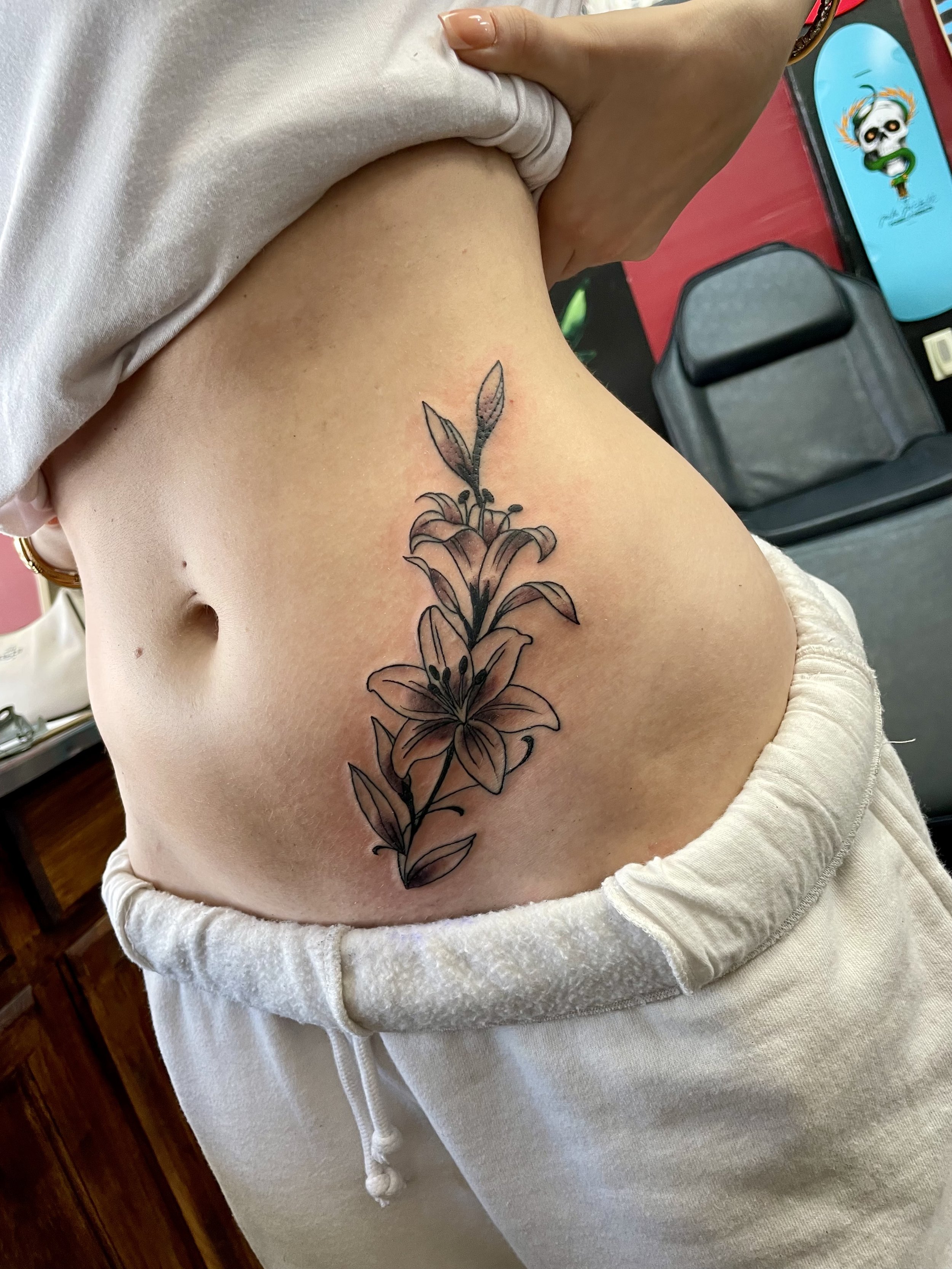 Fine line black and grey tiger lily flower tattoo flowing along the stomach and hip, tattooed by Nick Richard at Big Kahuna Tattoo in Boca Raton, FL