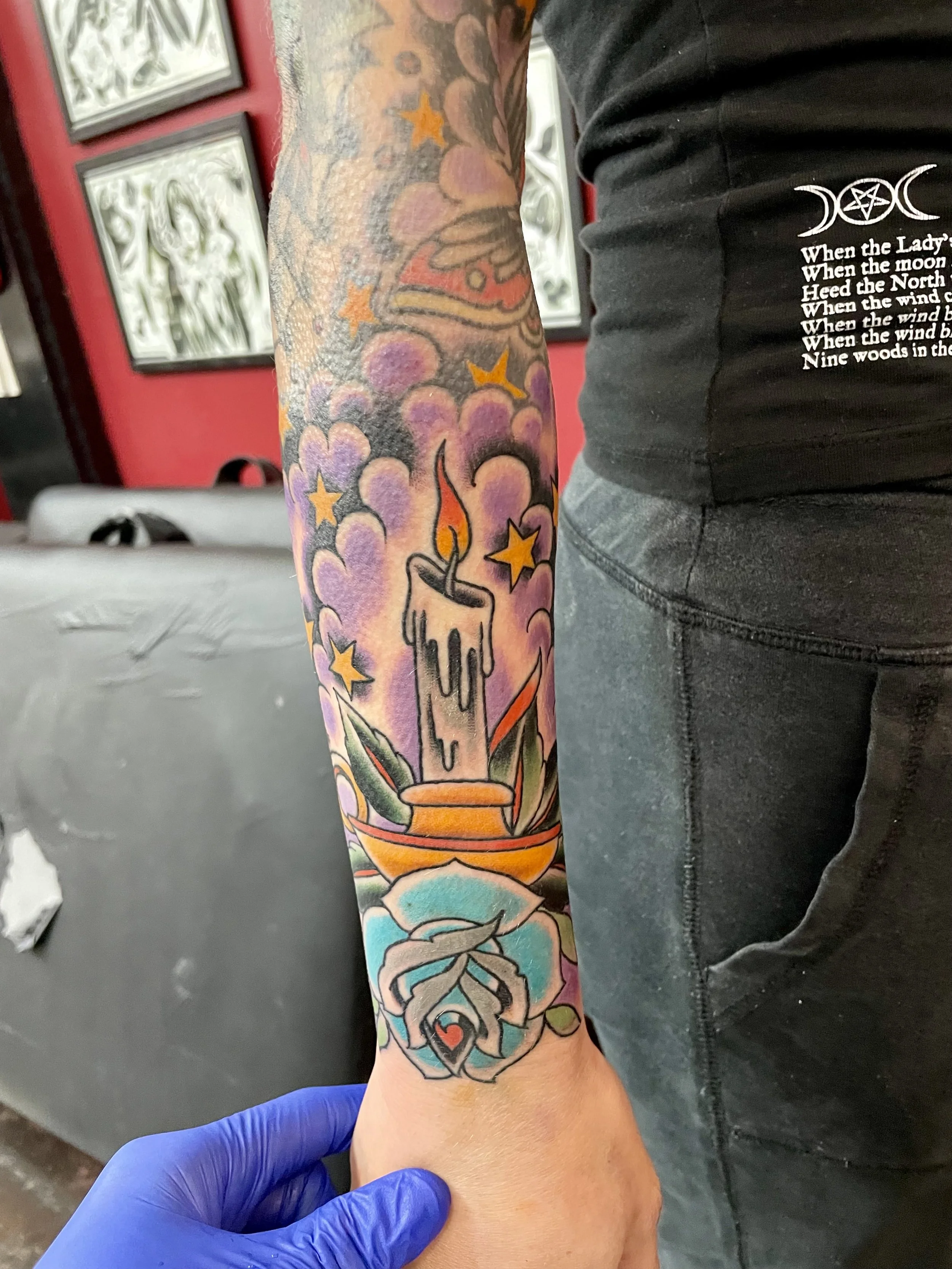 A dripping candle on a gold holder sits above a pale blue rose, surrounded by gold stars and soft purple clouds. Witchy, warm, and completely unique. Color forearm tattoo by Nick at Big Kahuna Tattoo in Boca Raton, FL.