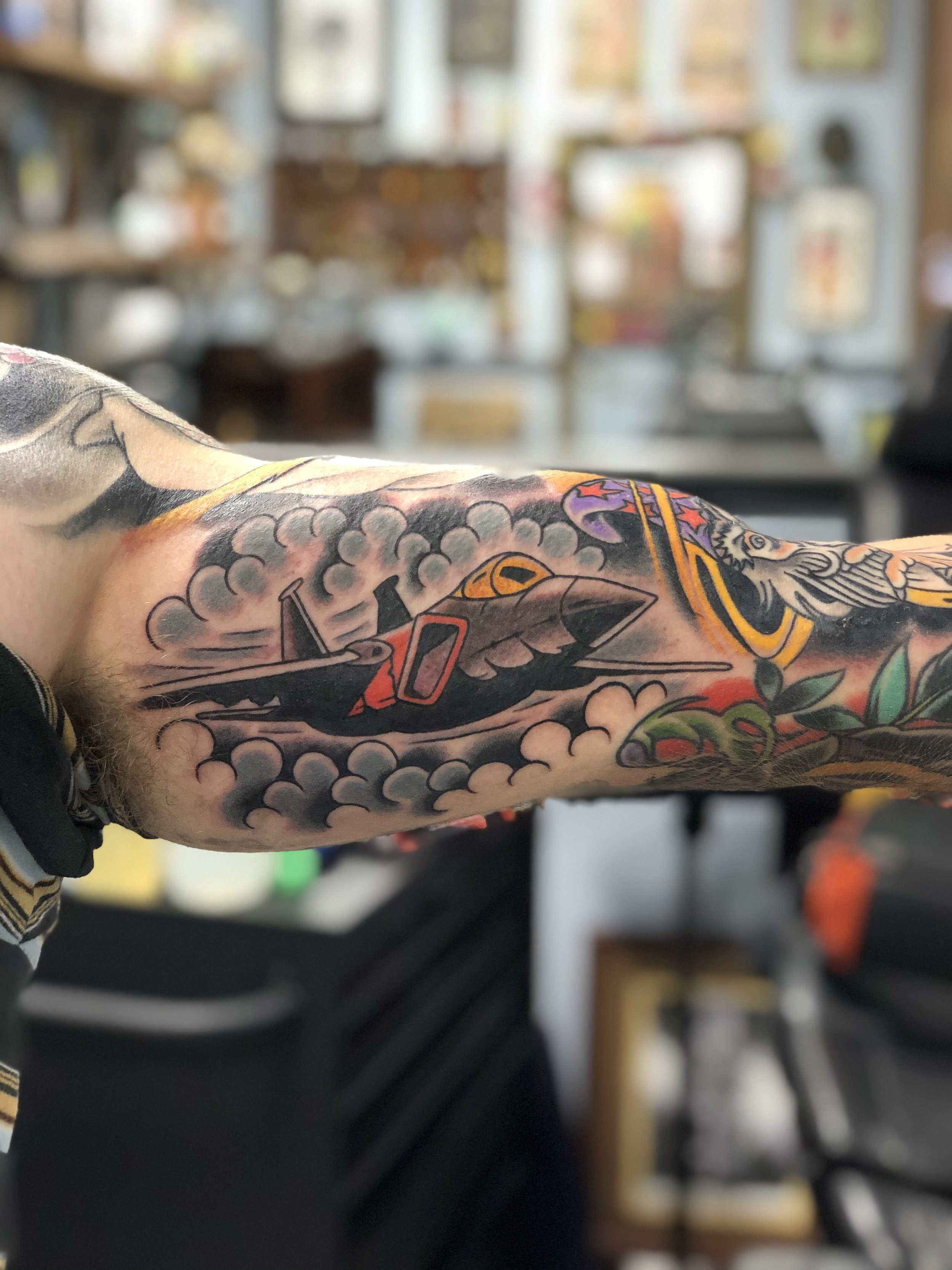 Traditional American color sleeve panel tattoo featuring a military fighter jet breaking through storm clouds, part of a larger arm sleeve, custom tattoo by Nick at Big Kahuna Tattoo in Boca Raton, FL.