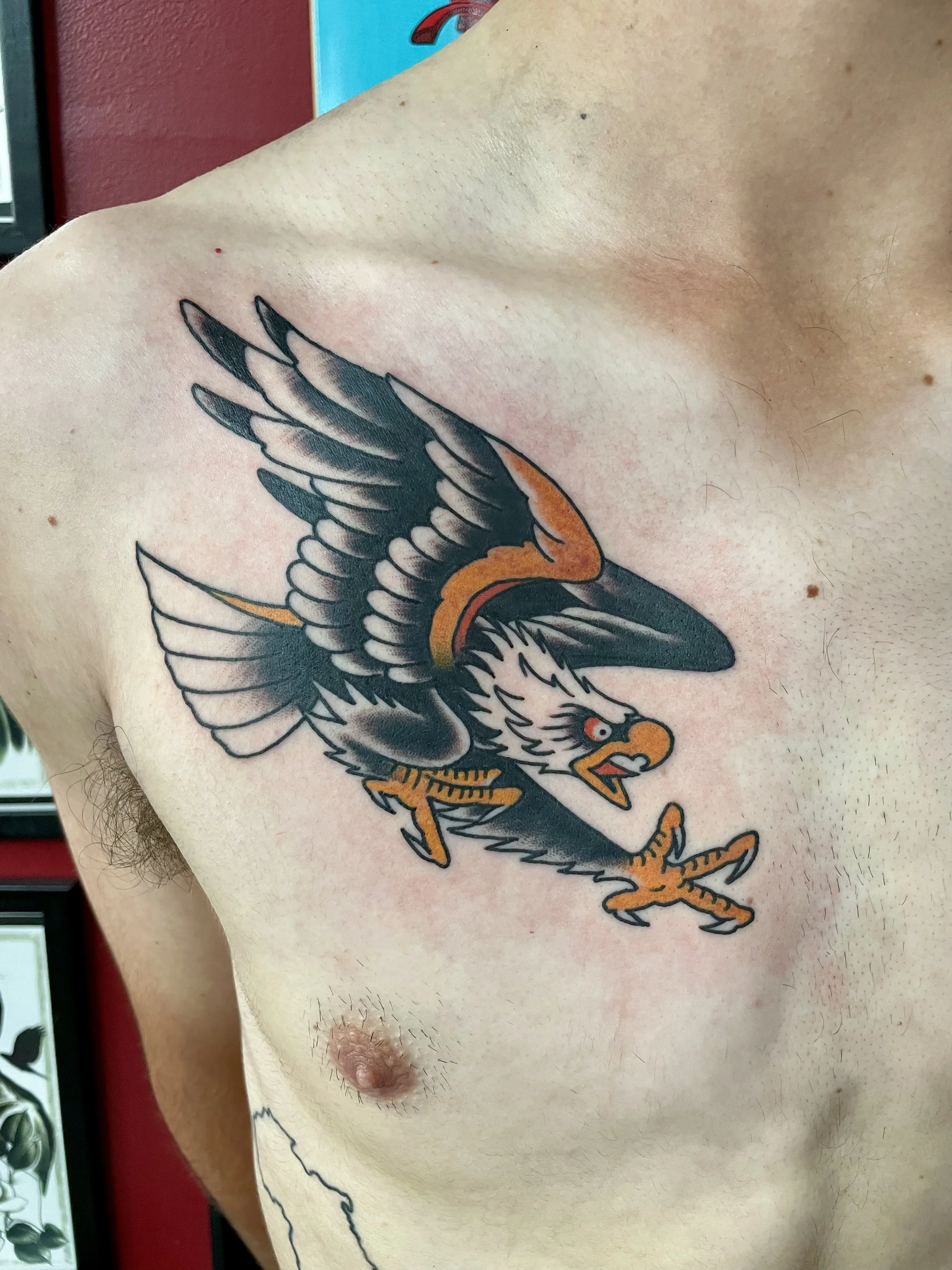 Traditional American color chest tattoo featuring a bold diving bald eagle with wings swept back, white head feathers, red eye, and gold talons extended in a striking attack pose, custom tattoo by Nick at Big Kahuna Tattoo in Boca Raton, FL.