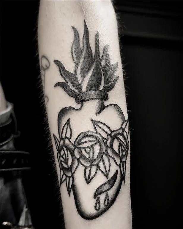 Black and grey traditional forearm tattoo featuring a sacred heart with flames and roses in a religious devotional style, custom tattoo by Brandon Perez at Big Kahuna Tattoo in Boca Raton, FL