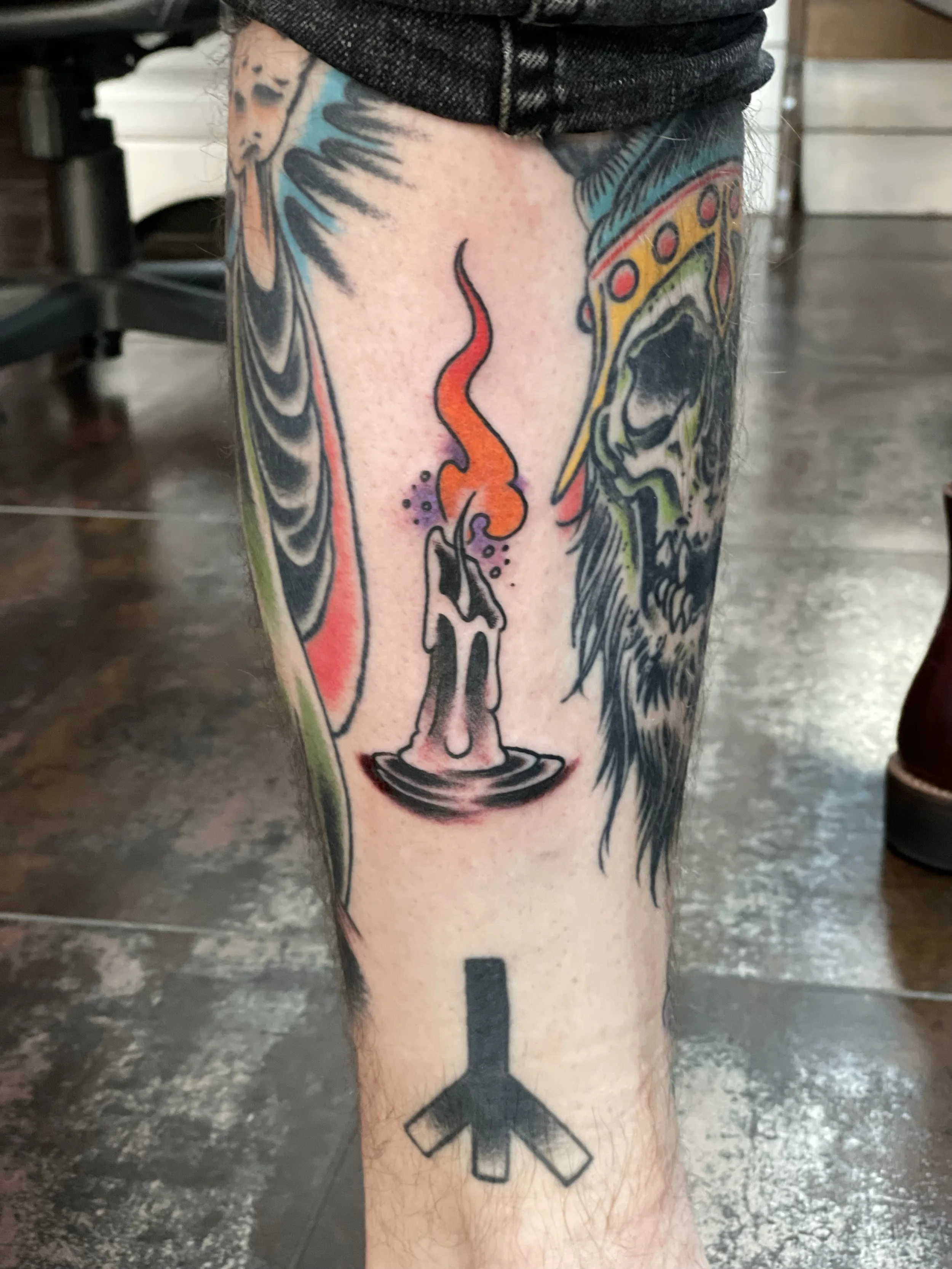 Color shin tattoo featuring a melting candle on a dish with a vivid orange and red flame, set among an existing leg sleeve, custom tattoo by Nick at Big Kahuna Tattoo in Boca Raton, FL