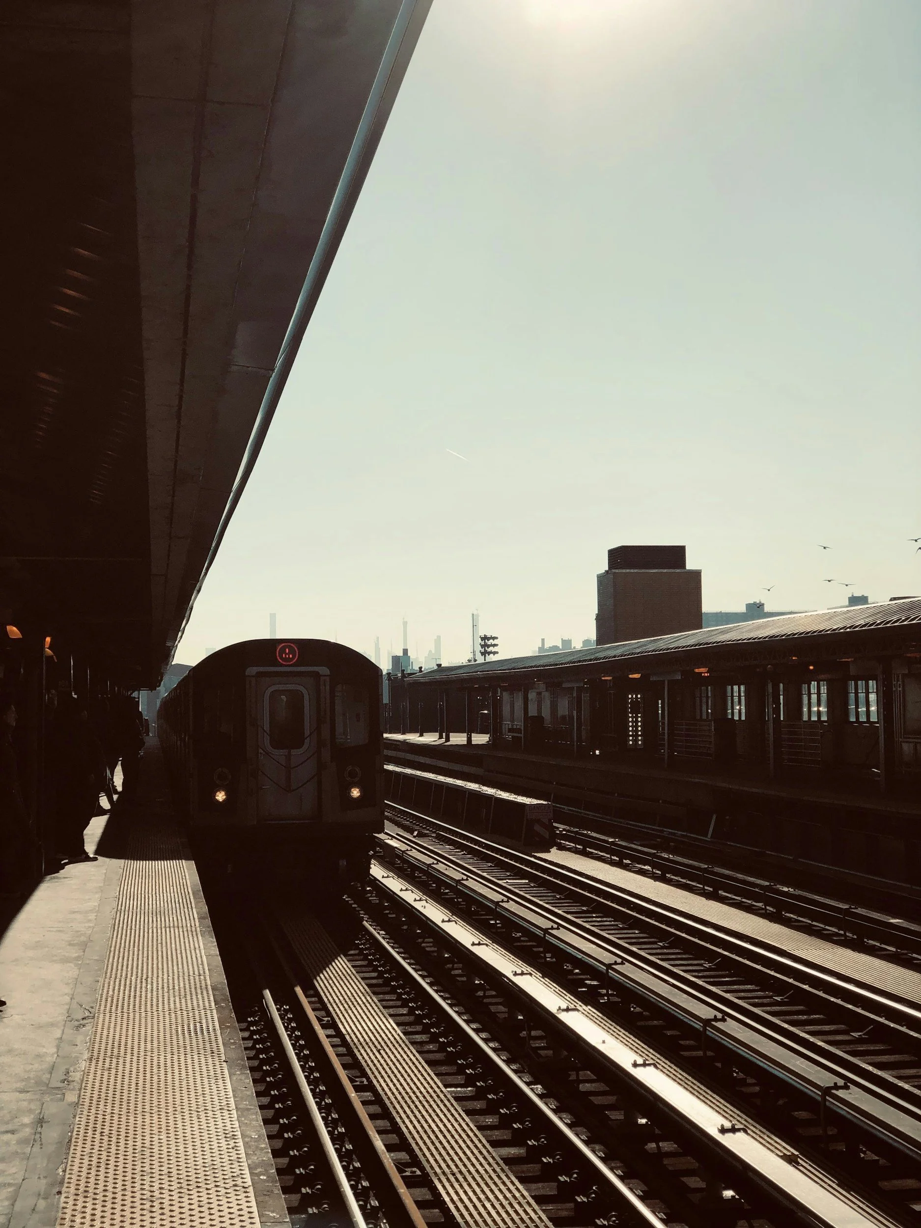 Subway train arriving at an elevated train station in an urban area with city skyline in the background.