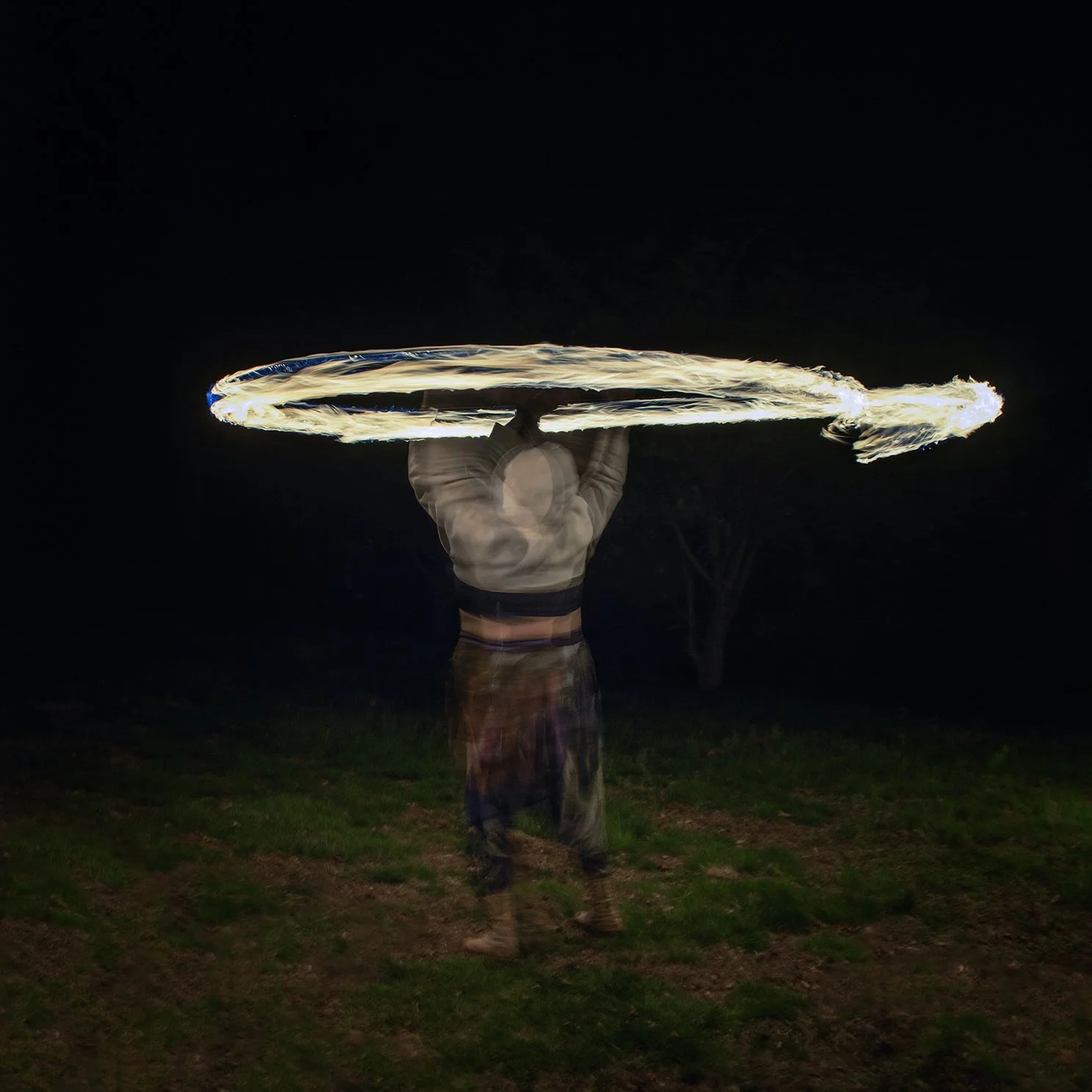 A person performing fire spinning with a puppy hammer prop at night, creating circular fire trails.