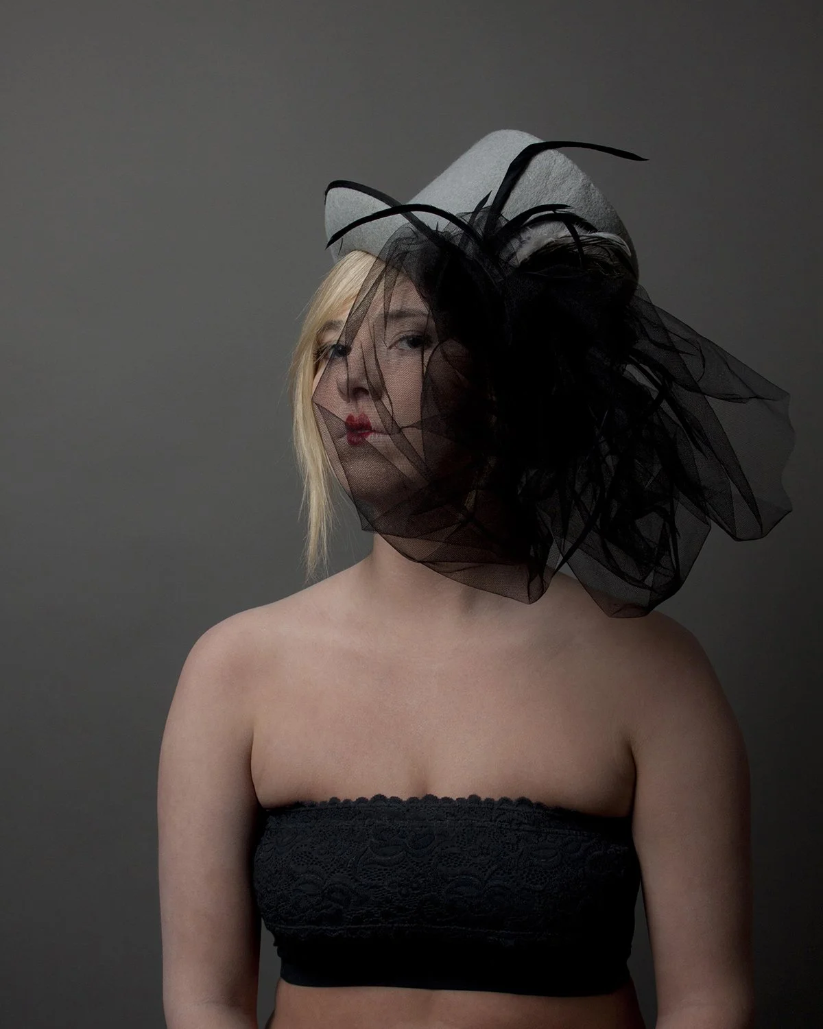 Studio portrait of a woman wearing a large top hat, decorated with a vail that partially obscures her face.