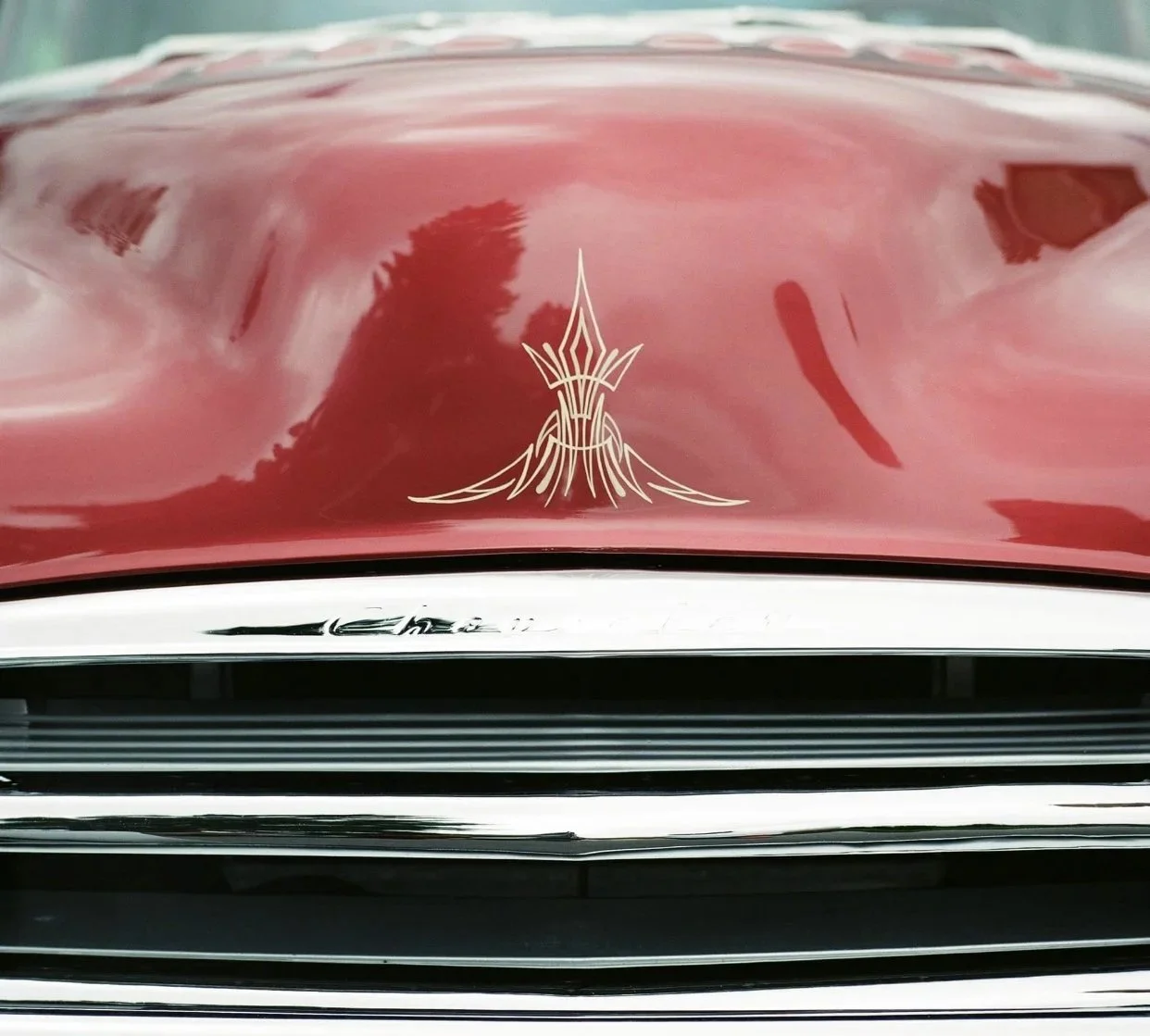 Close-up of a vintage red car's hood with pin stripe detail and a chrome grille.