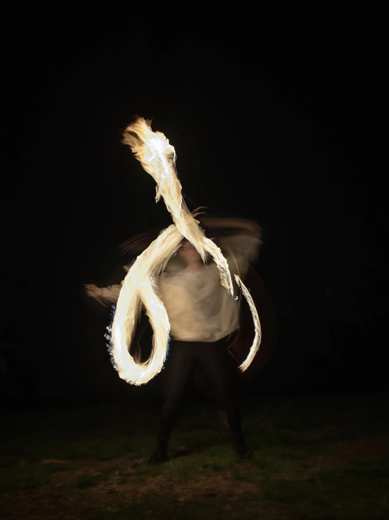 Person performing poi fire spinning at night, creating a dragon form looping light trail through long exposure photography.