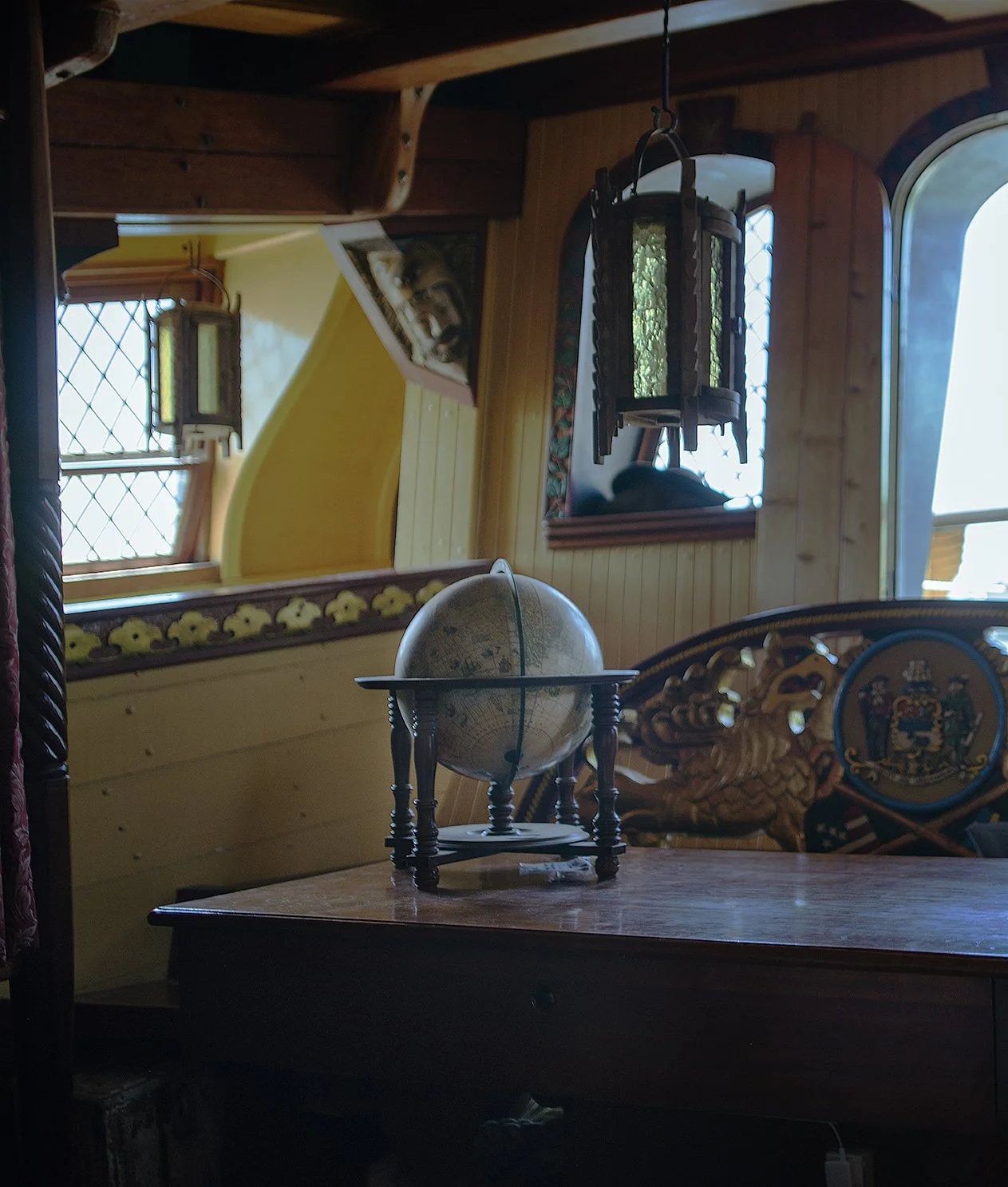 A vintage globe on a small wooden table inside a cozy room with wooden paneling, windows, and decorative antique items.