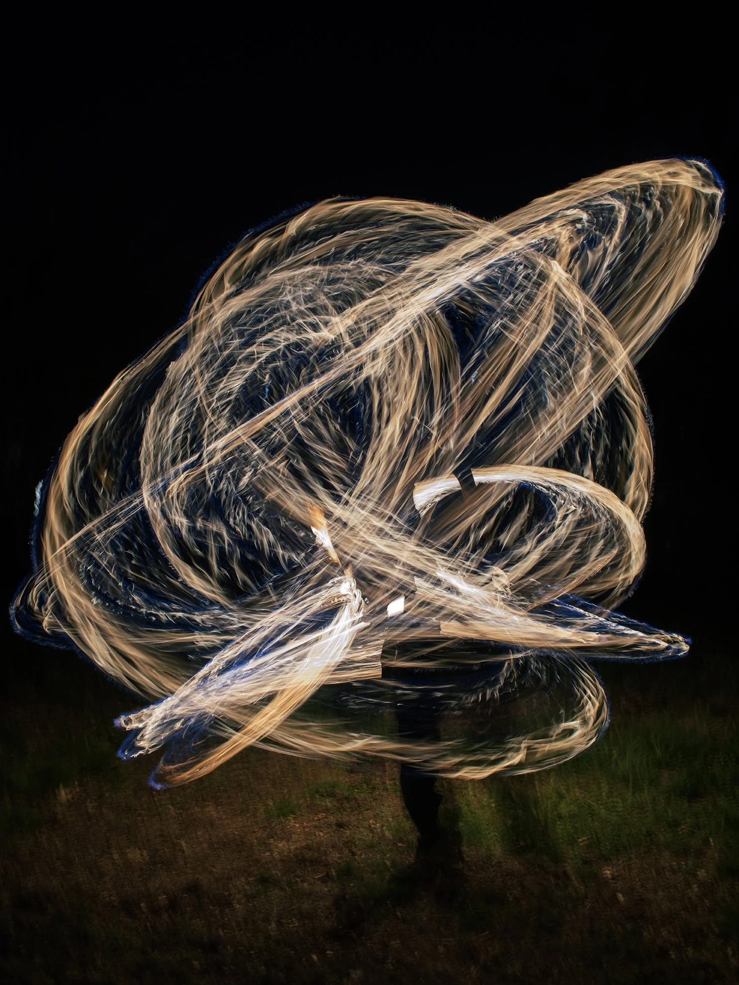 Light painting with swirling, glowing trails against a dark background, with a faint figure visible at the bottom.