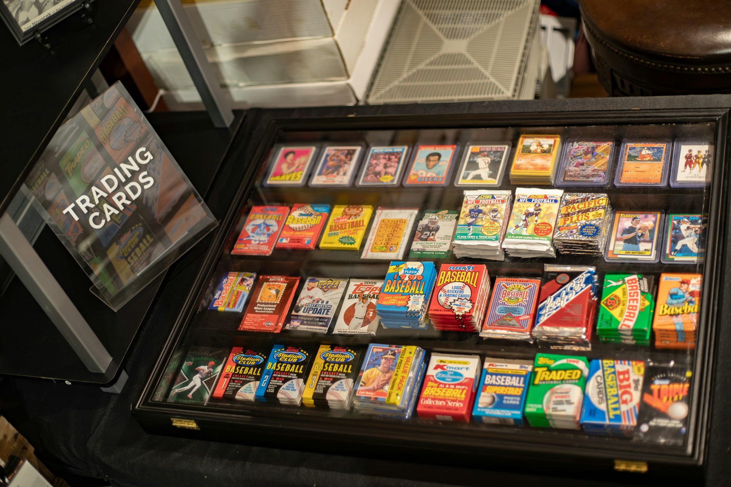 A display case with vintage baseball, football, basketball, and trading cards, along with a sign labeled 'Trading Cards'.