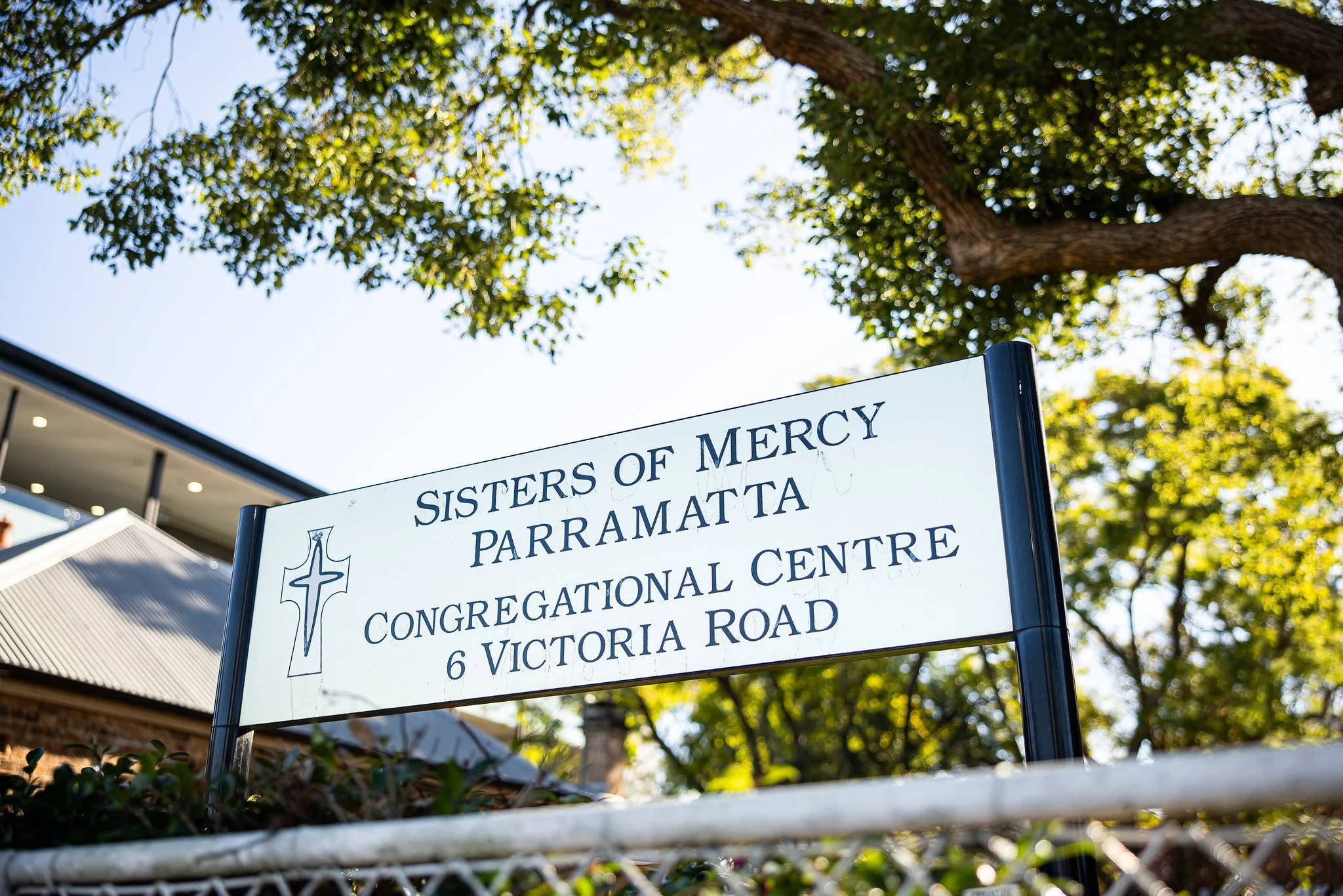 Sign for Sisters of Mercy Parramatta Congregational Centre at 6 Victoria Road, with green trees and part of a building in the background.