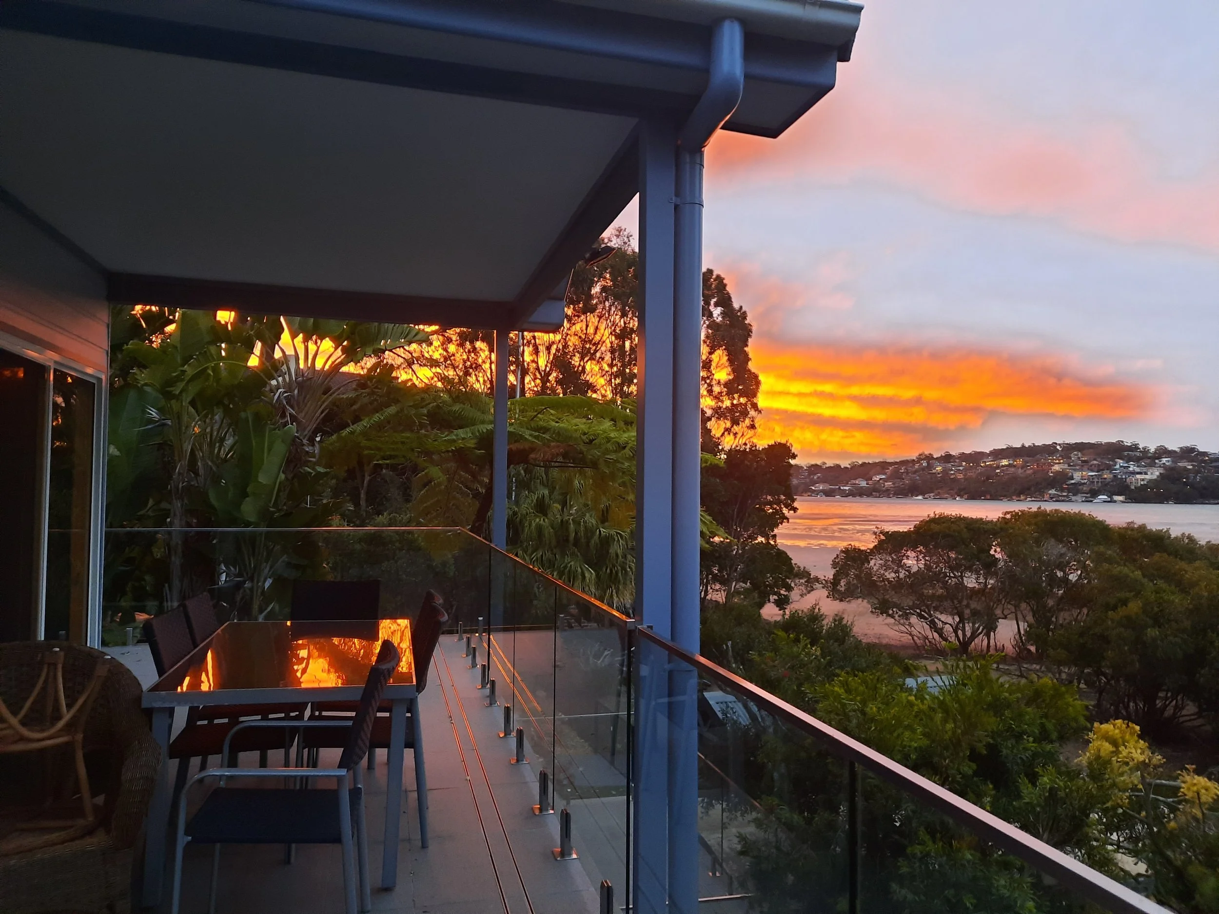 A balcony overlooking a lush landscape with trees and a river, during a vibrant sunset with orange and pink clouds.