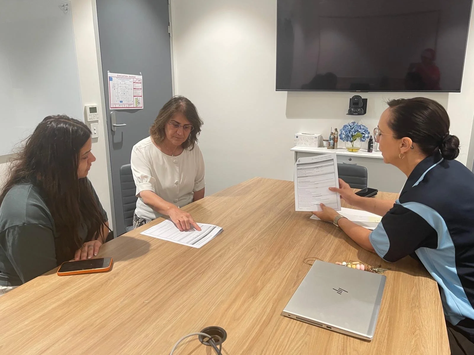 Three women meeting in a conference room, with papers and a laptop on the table.