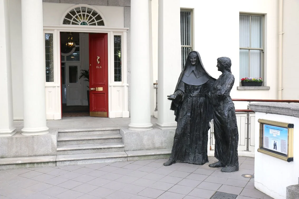 Bronze statue of a nun and a man standing outside a building with a red door and white columns.