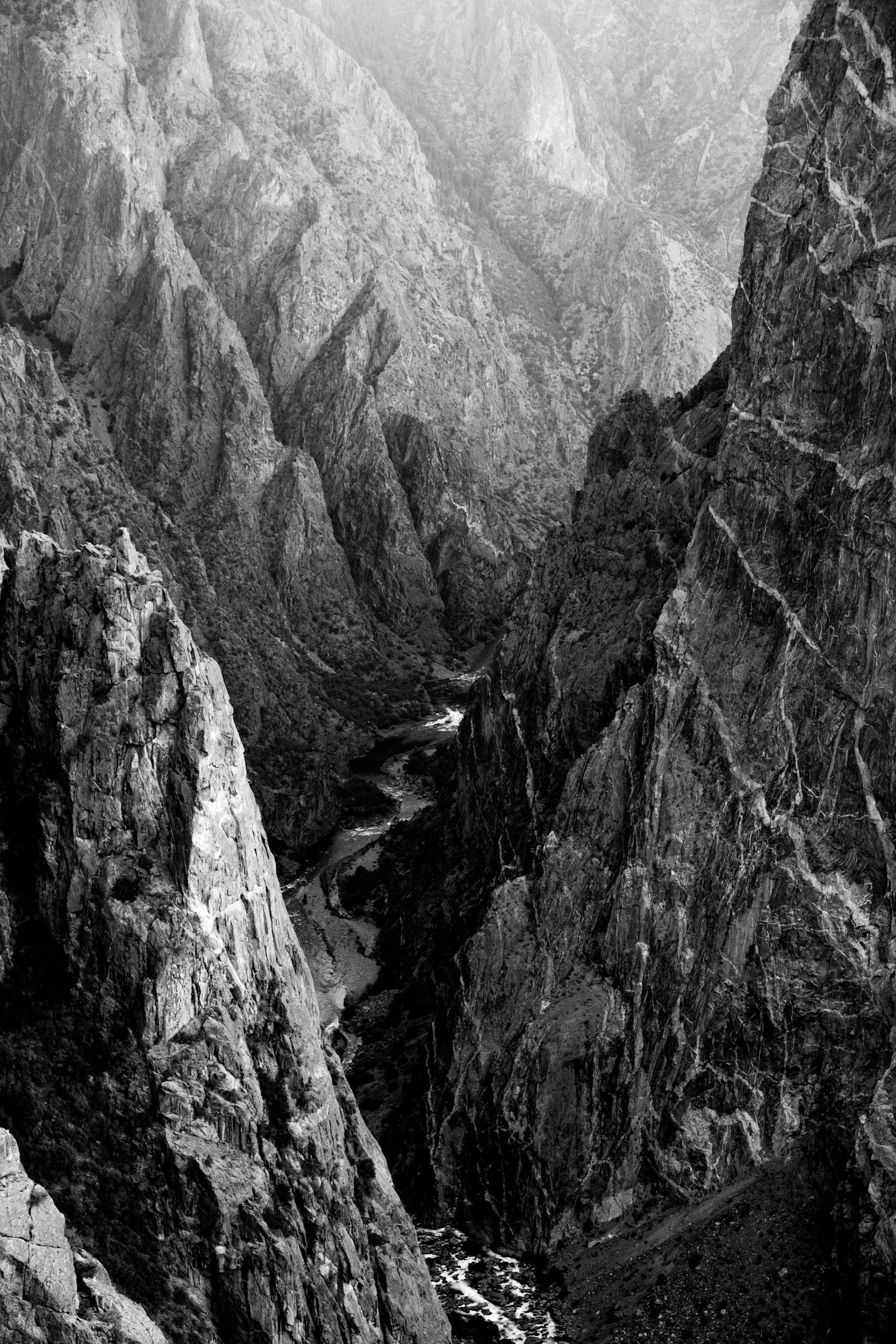 Black and white photo of a deep canyon with steep rocky walls and a river flowing at the bottom.